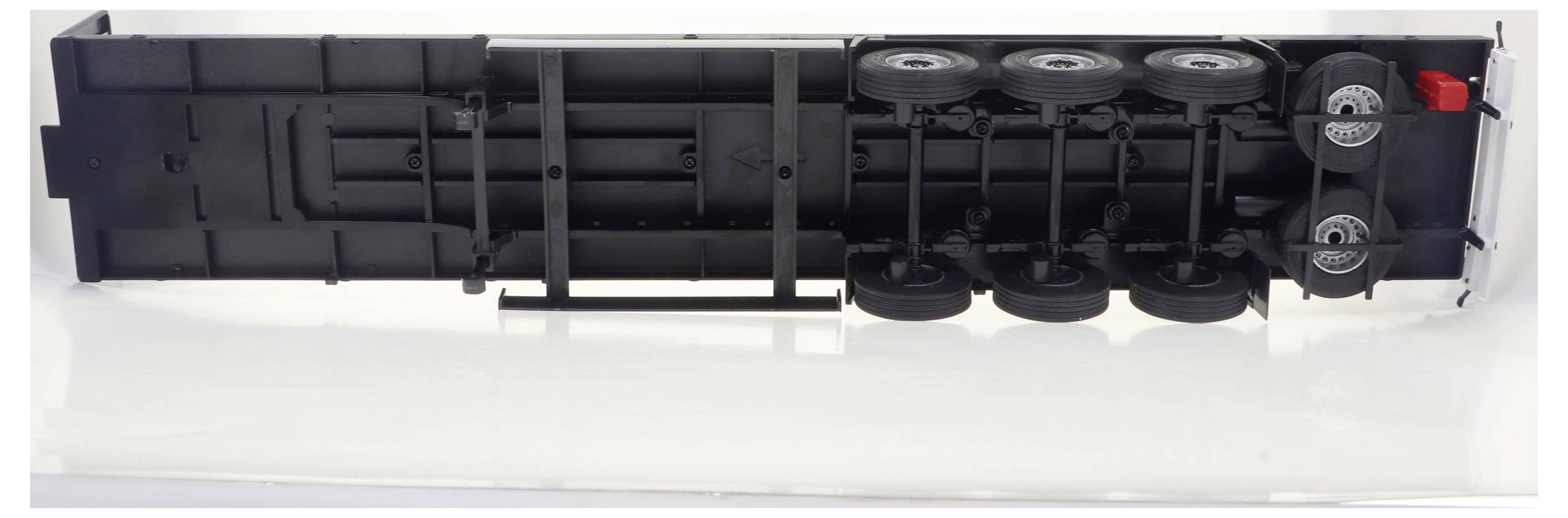 Czarny przyczep ciężarówki leży przewrócony na bok, z widocznymi kołami i czerwonym detalem na jednym z końców.