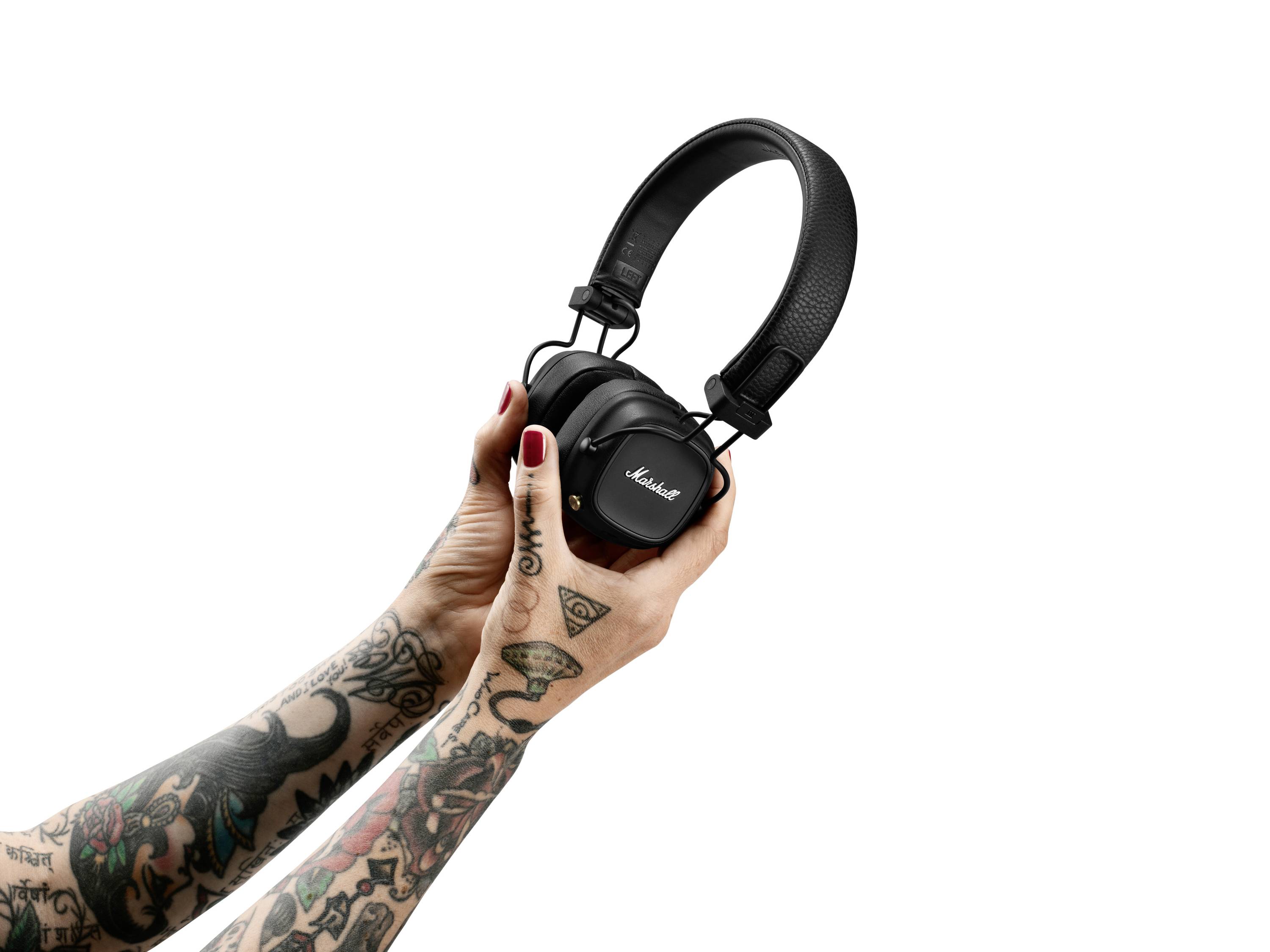 Dwie wytatuowane dłonie trzymają czarne słuchawki studyjne na białym tle.