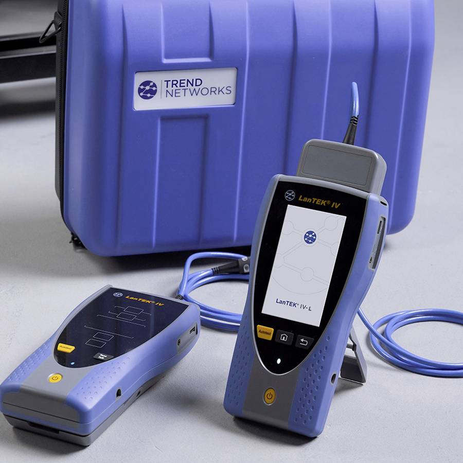 Dwa urządzenia testowe sieci z wyświetlaczami i kablami przed niebieskim futrafem z napisem 'TREND NETWORKS'.