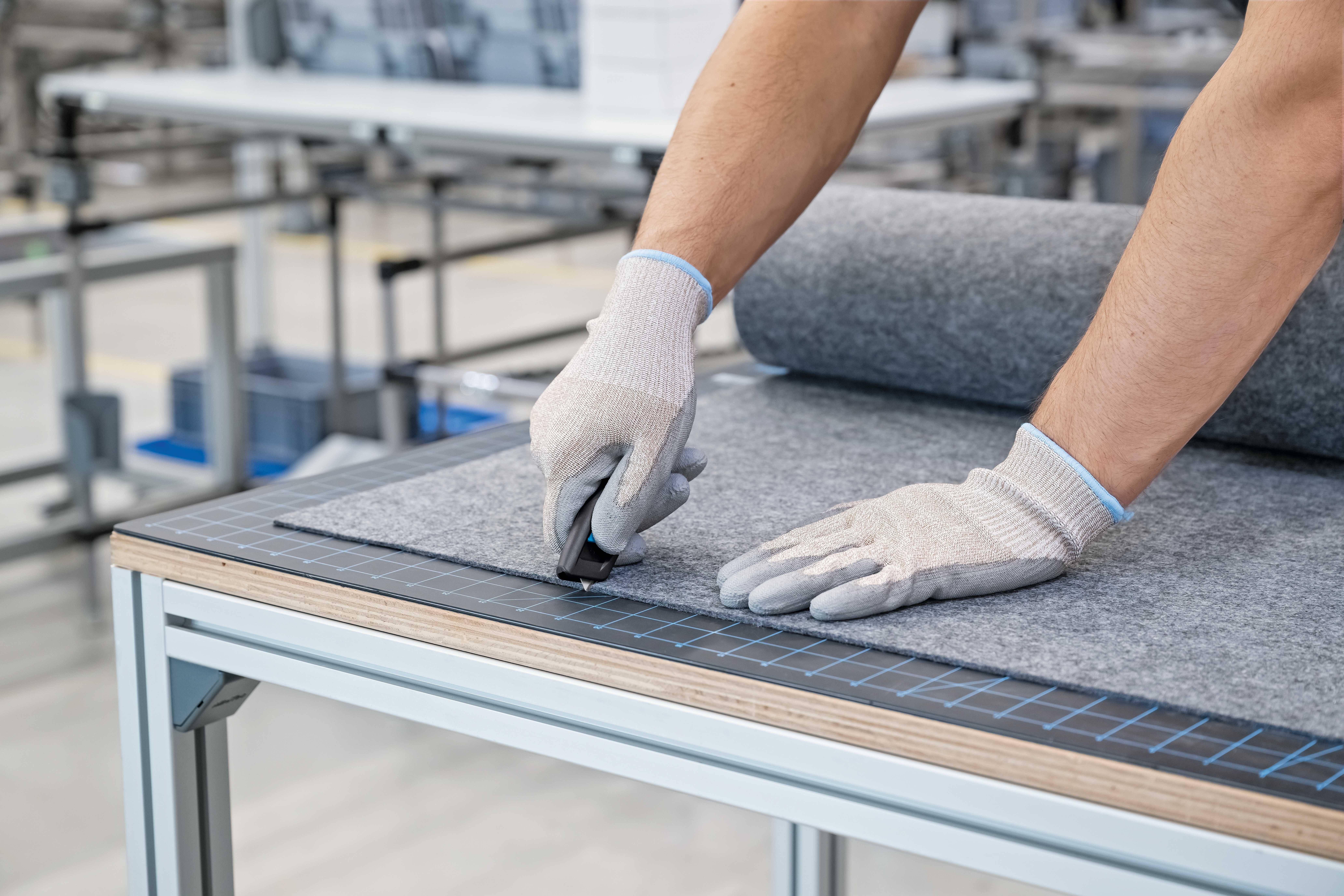 Osoba kroi filc na profesjonalnym stole roboczym za pomocą noża introligatorskiego. Nosi rękawice ochronne.