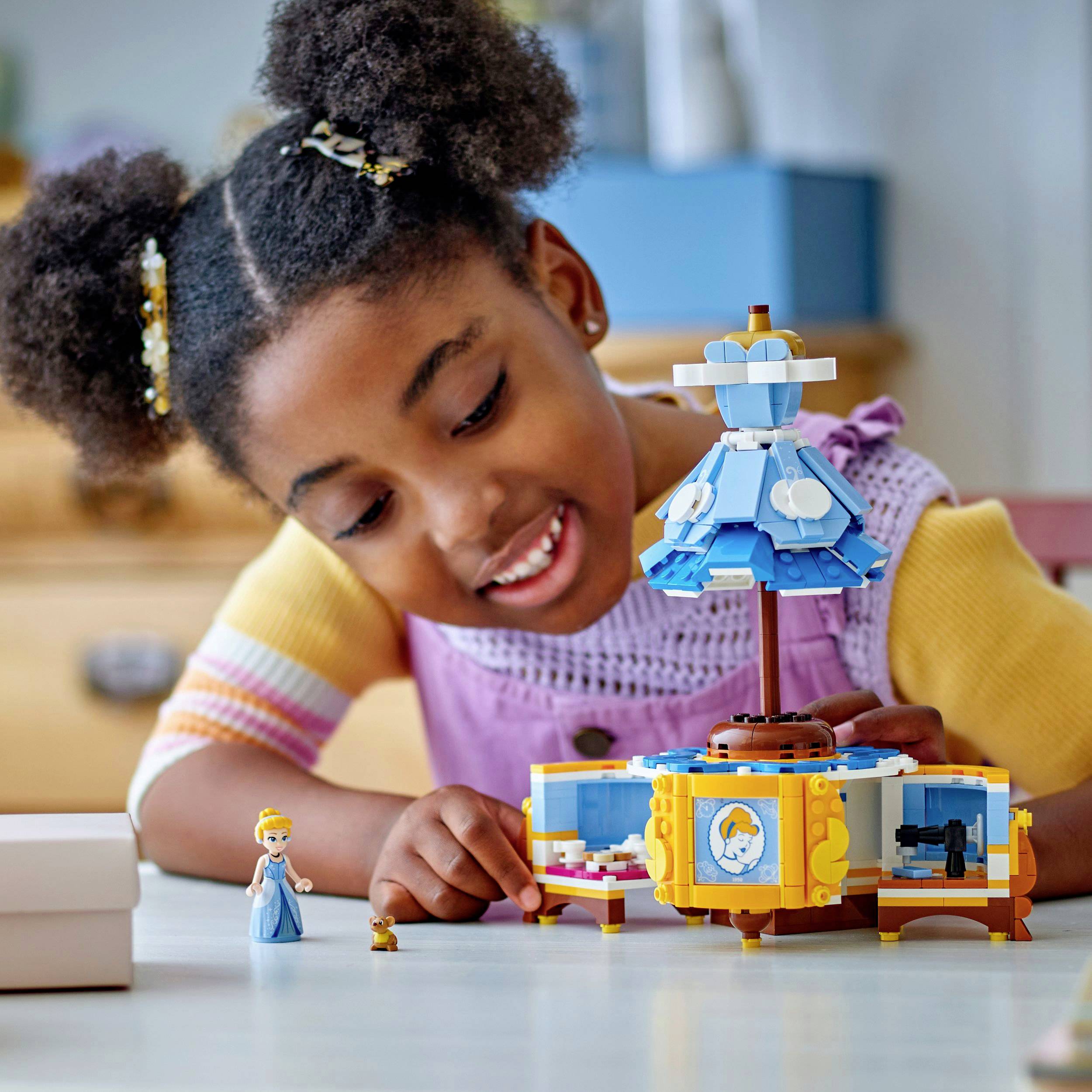 Dziecko radośnie bawi się zamkiem zabawkowym i małą figurką księżniczki na stole. W tle stoją meble.