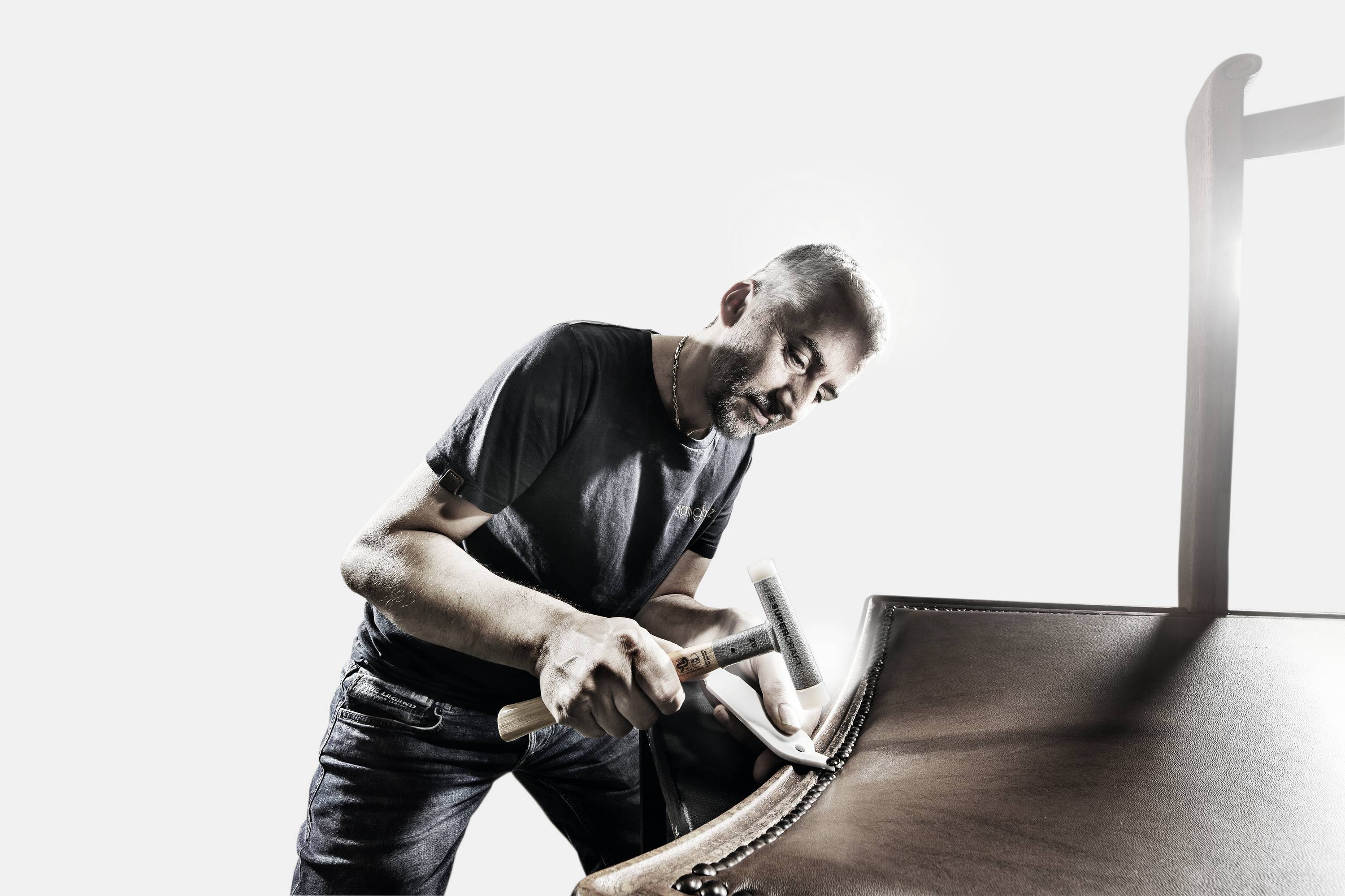 Rzemieślnik starannie naprawia drewniane krzesło, wbijając gwoździe wzdłuż krawędzi.