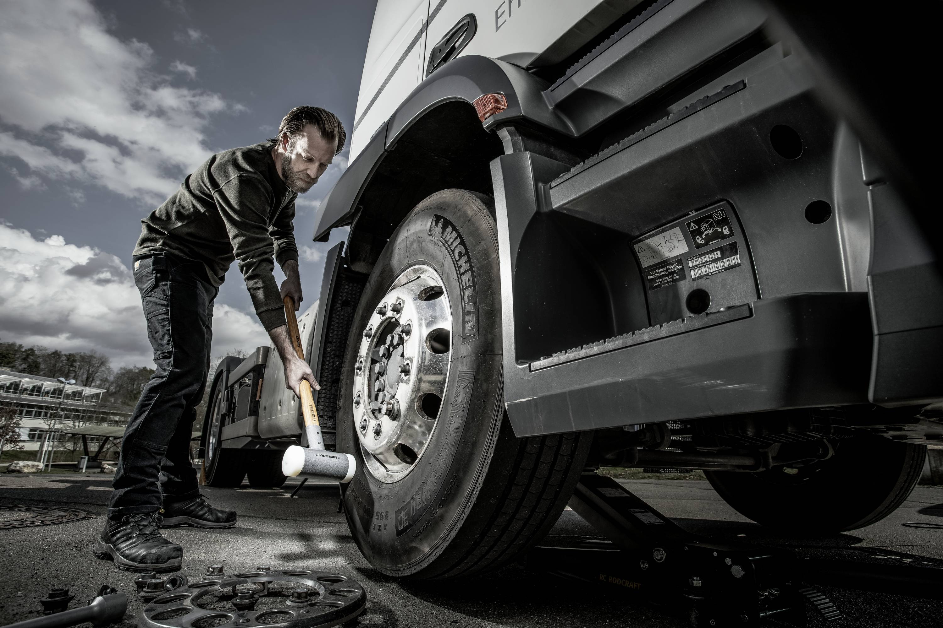 Mężczyzna sprawdza ciśnienie w oponach ciężarówki za pomocą młotka na parkingu.