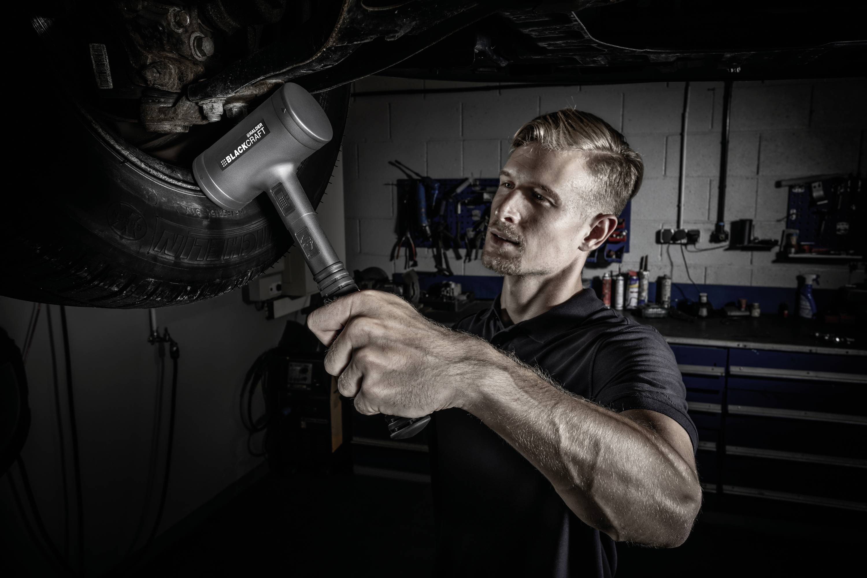 Mechanik pracuje w warsztacie i używa młotka gumowego do naprawy części samochodowej.