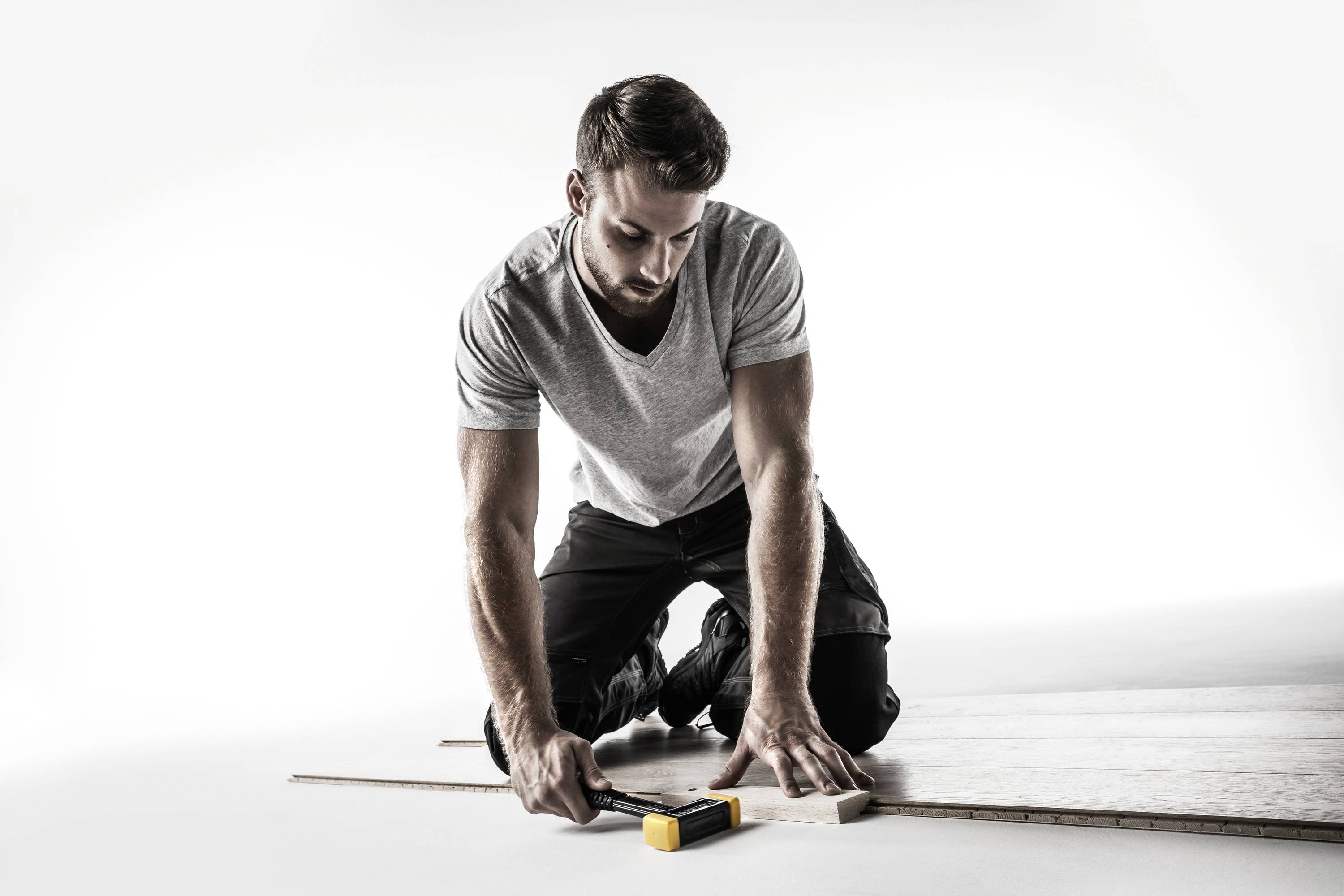 Mężczyzna klęczy na podłodze i mierzy deskę drewnianą za pomocą miarki.