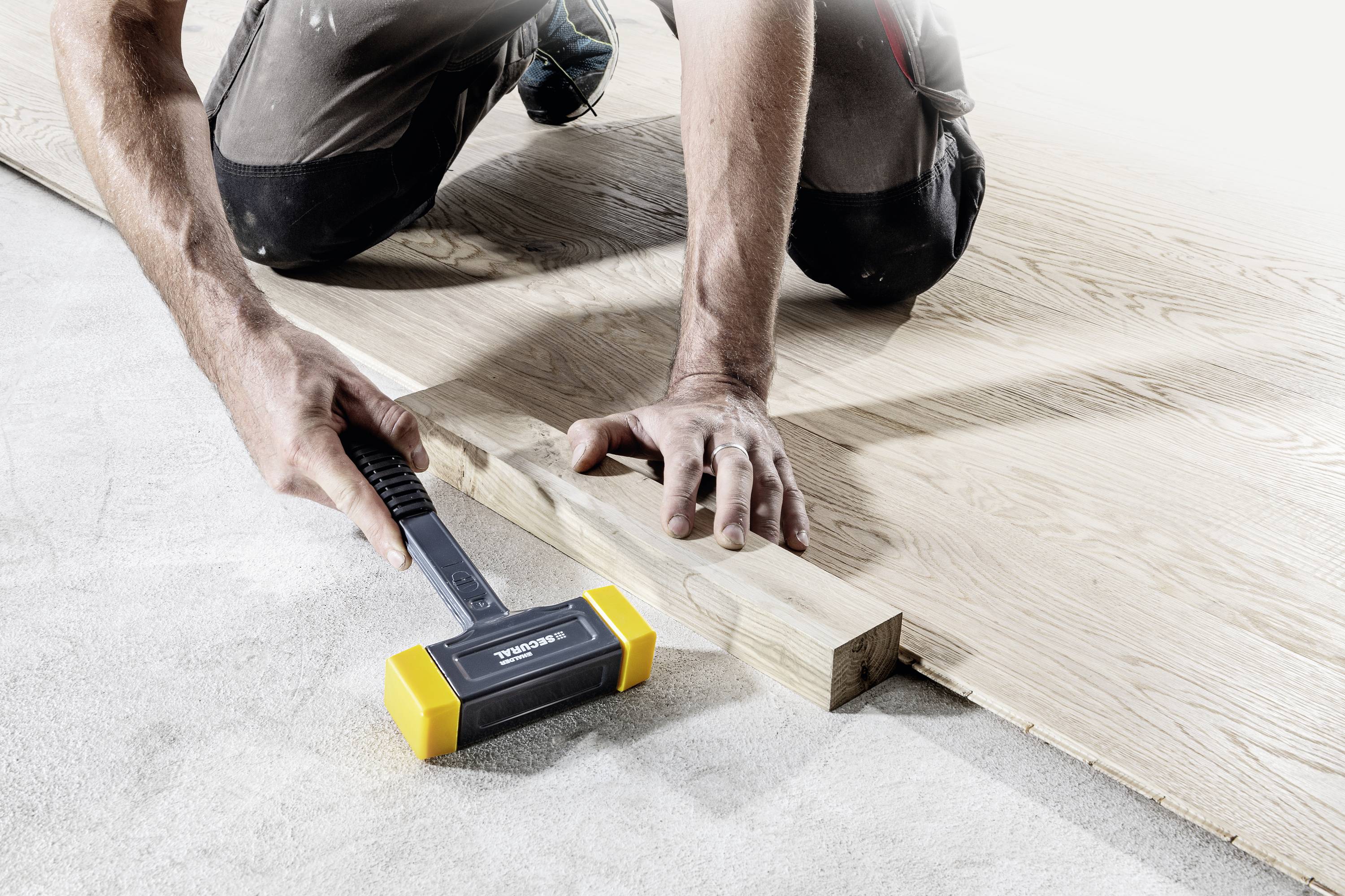 Osoba montuje podłogę laminowaną, używając gumowego młotka do precyzyjnego umieszczania paneli. Ręce i narzędzie są w centrum kadru.