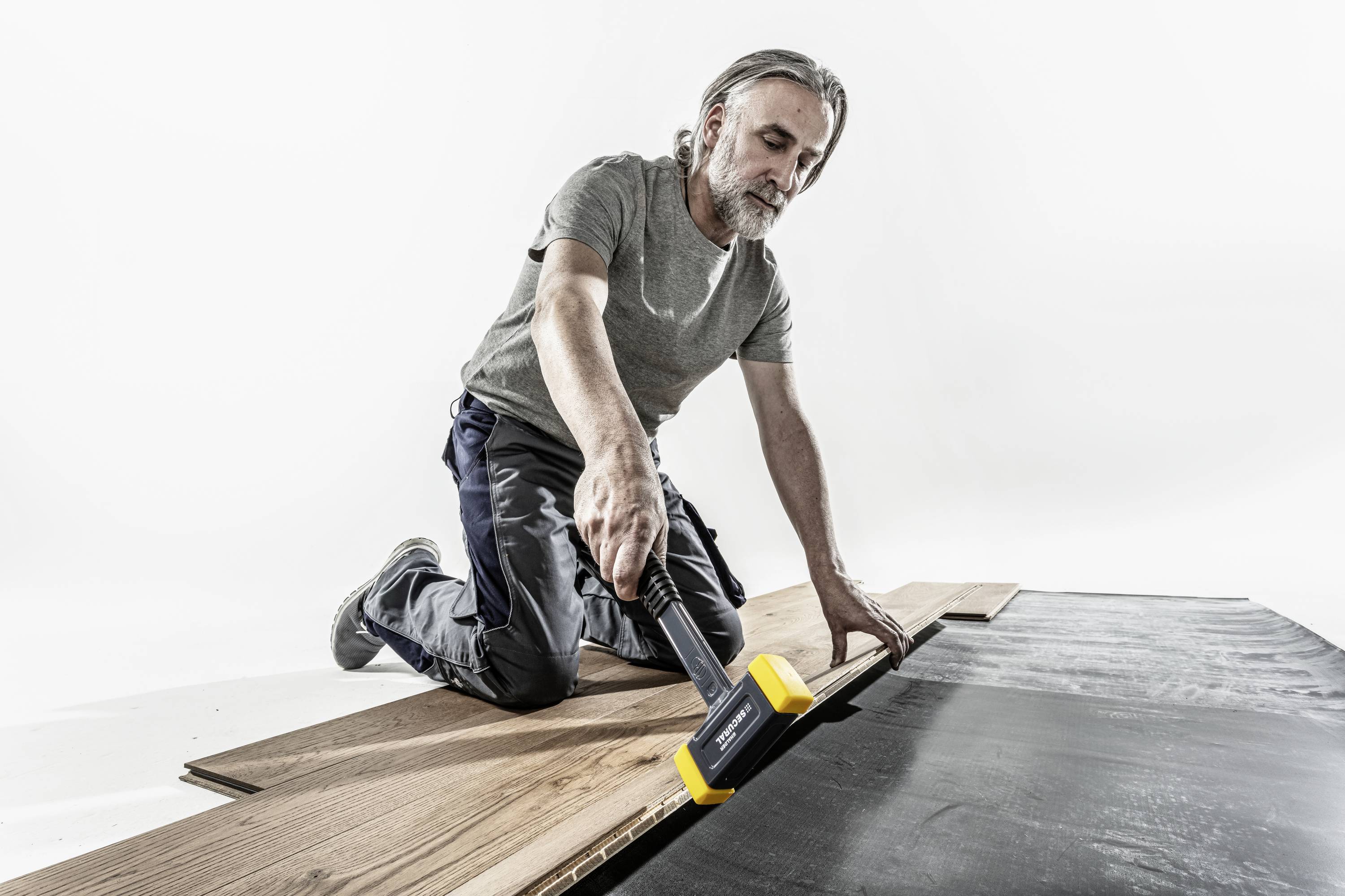 Mężczyzna klęczy na podłodze i układa panele laminowane za pomocą młotka.