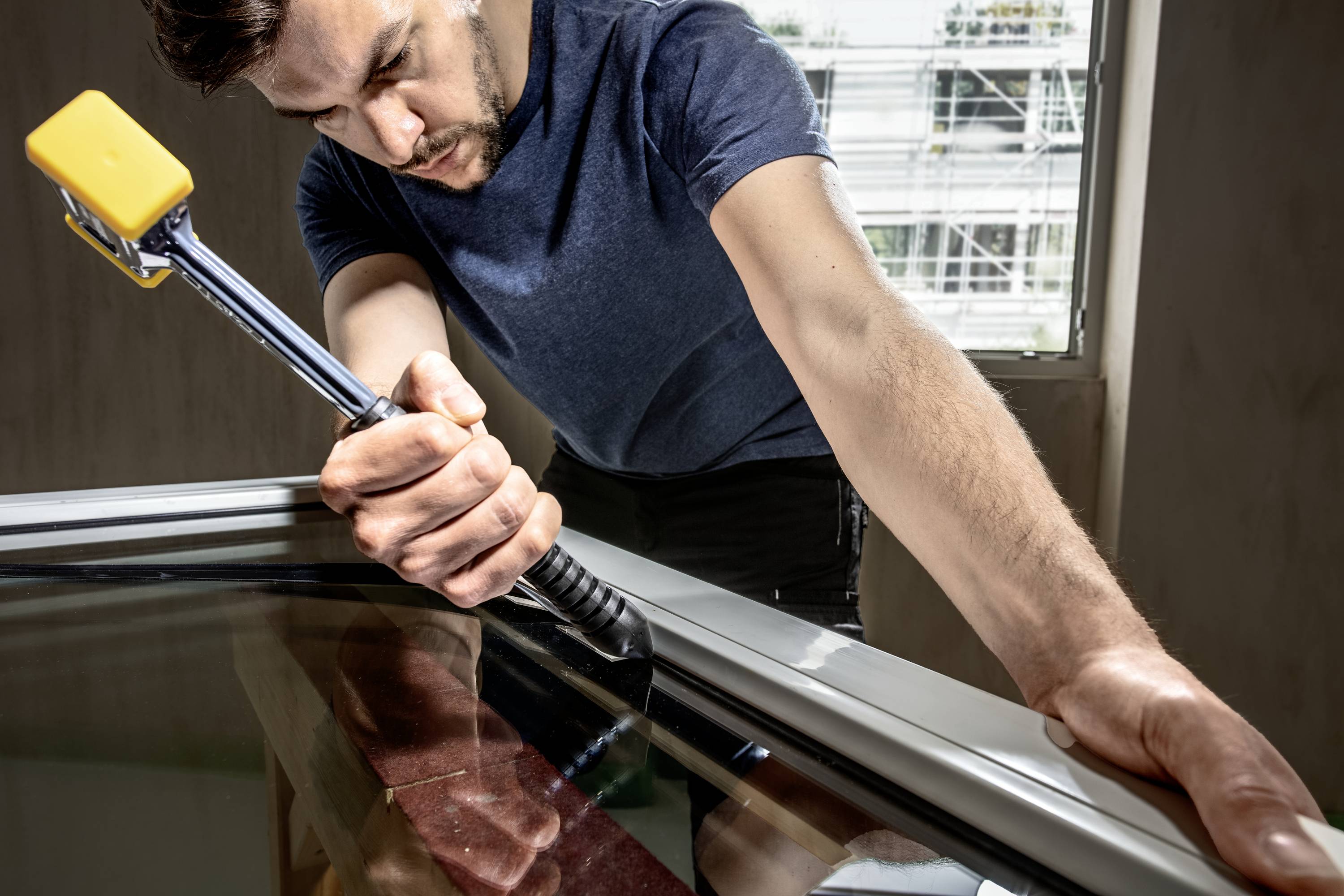 Mężczyzna używa narzędzia, aby naprawić lub dopasować szybę lub szklany element. Jest całkowicie skoncentrowany na wykonywanej pracy.