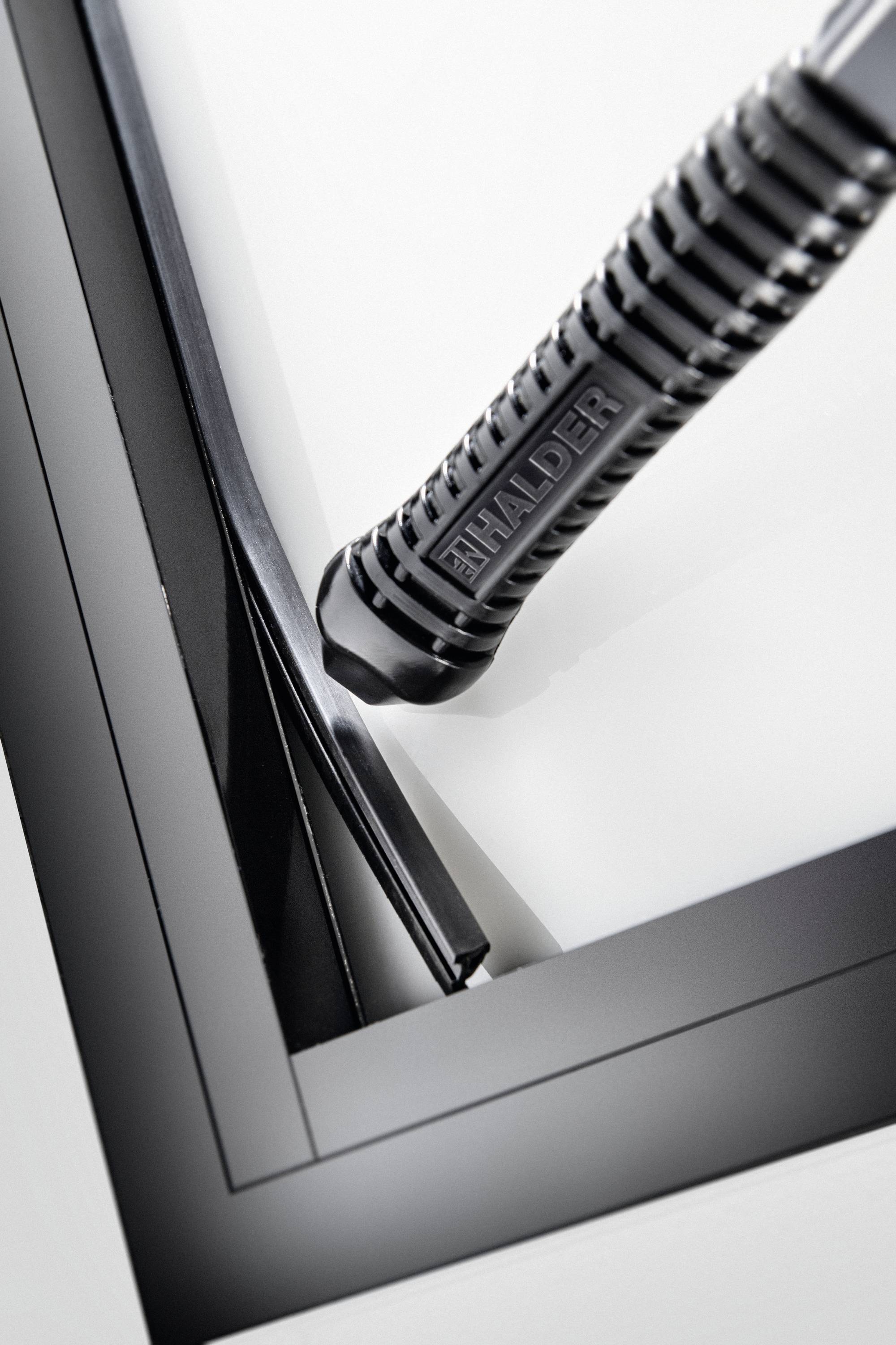 Czarny młotek z napisem 'HALDER' na szarym tle. Fokus skierowany jest na główkę młotka i jego rękojeść.