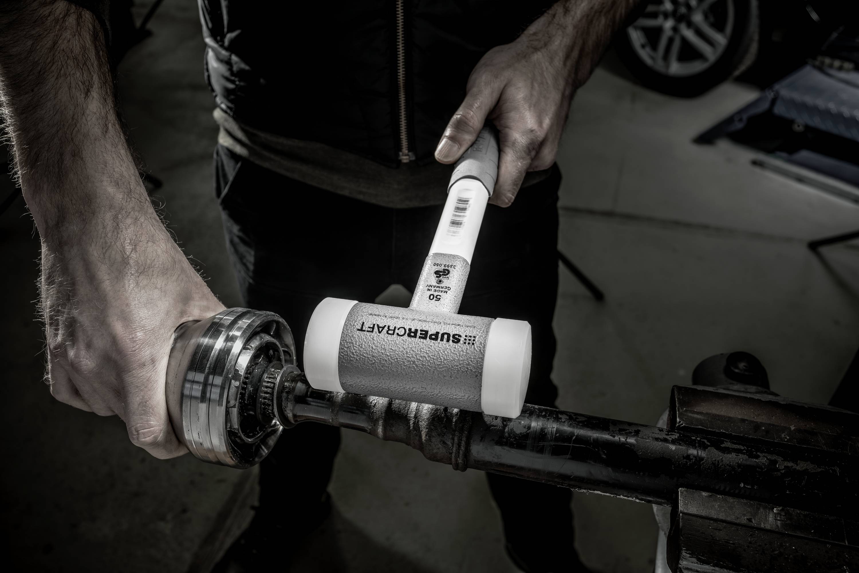 Osoba używa młotka gumowego, aby zamontować łożysko kulkowe na metalowym pręcie w warsztacie.