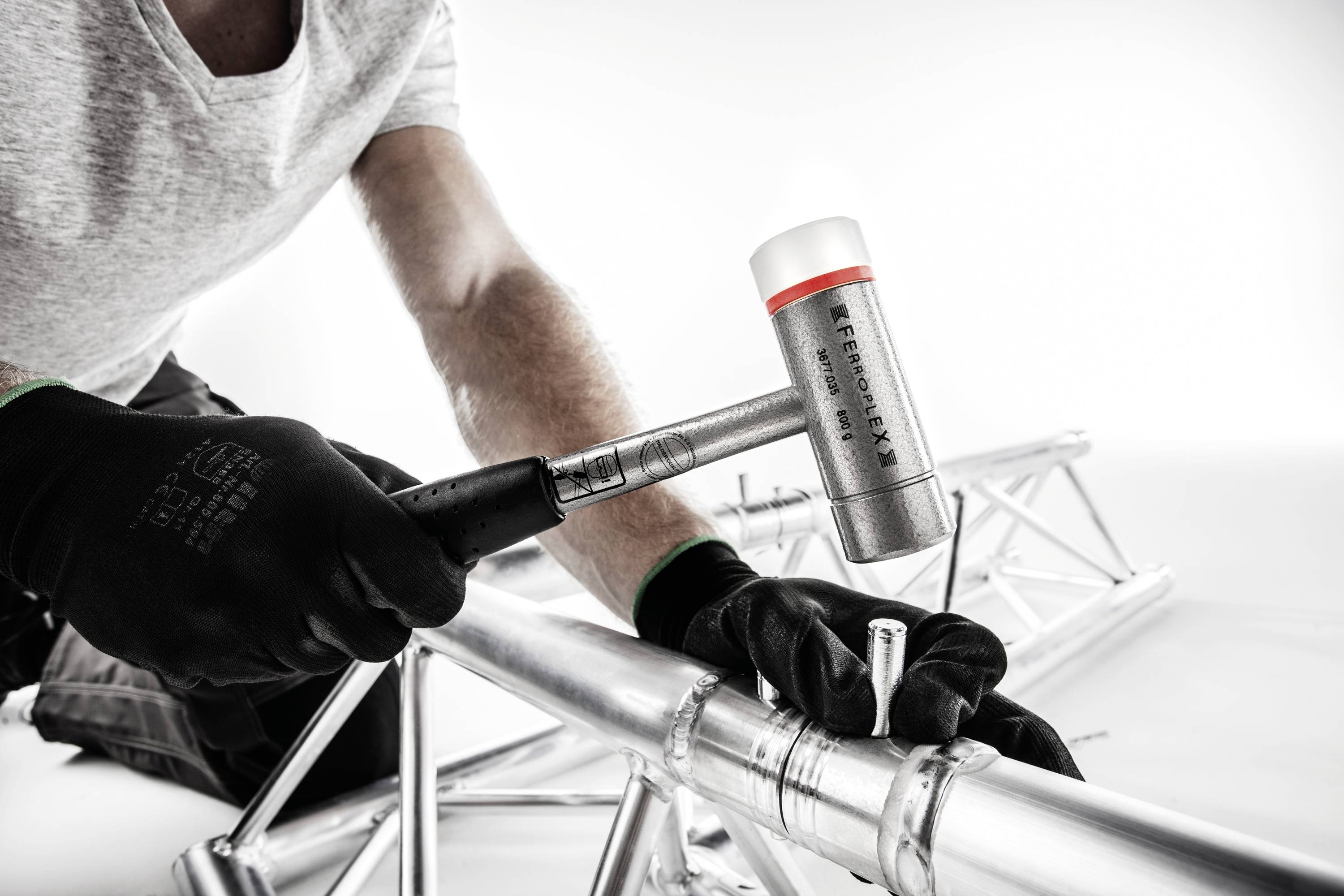 Osoba w czarnych rękawiczkach używa młotka do montażu srebrnej metalowej konstrukcji.