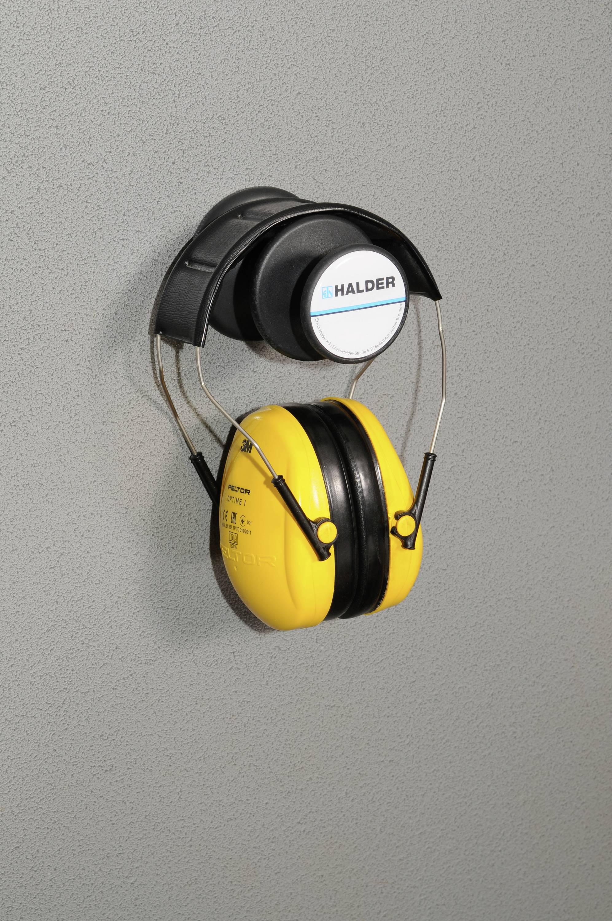 Żółta ochrona słuchu wisi na szarej ścianie.