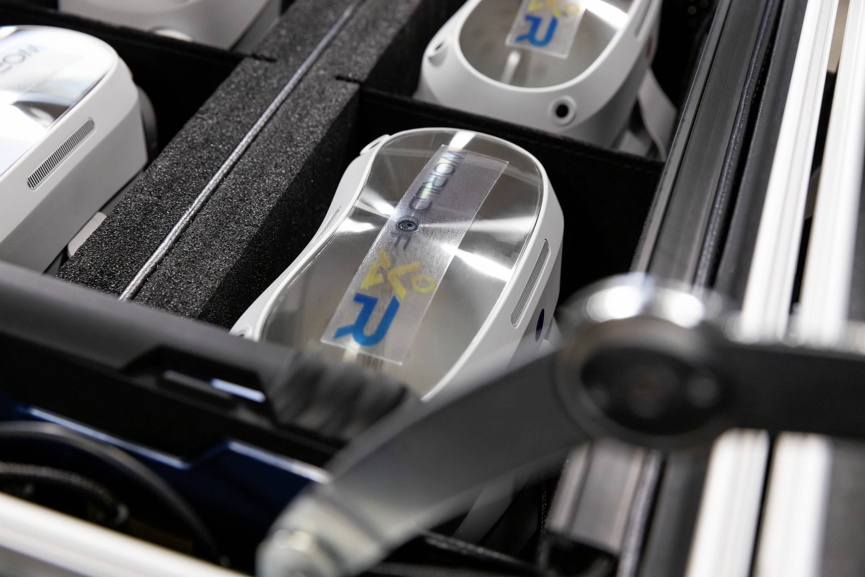 Walizka z kilkoma szarymi, owalnymi urządzeniami ułożonymi blisko siebie, z niebieskimi i żółtymi oznaczeniami na wierzchu.