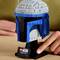 Kask LEGO Jango Fetta z filmu Star Wars jest prezentowany na stole. Ręka wskazuje na czarną tabliczkę z nazwiskiem.