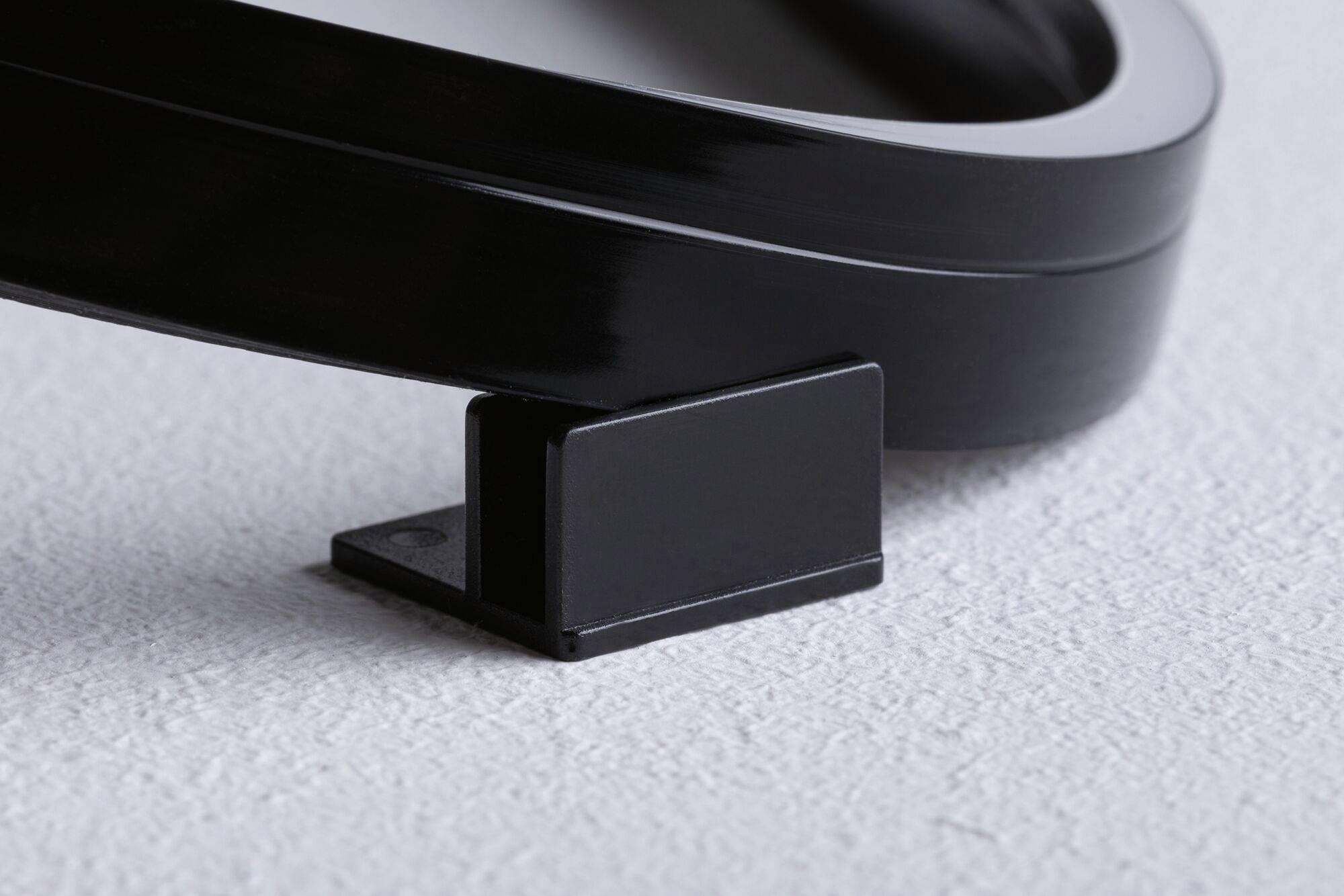 Czarny obiekt z tworzywa sztucznego na teksturowanym podłożu, prawdopodobnie będący częścią większego urządzenia lub mebla, o prostokątnej podstawie.