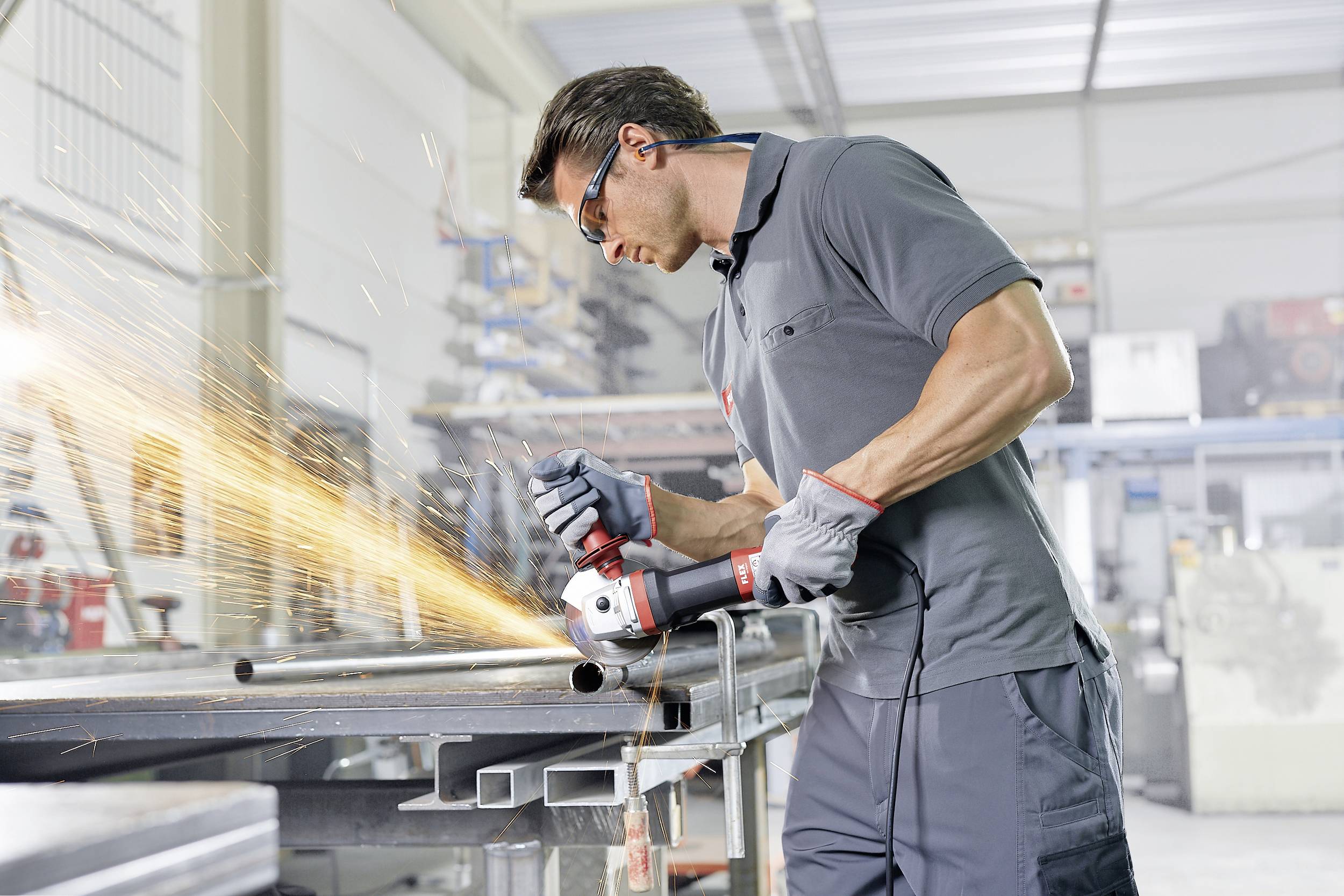 Mężczyzna szlifuje metal elektryczną szlifierką w warsztacie. Podczas procesu obróbki lecą iskry.