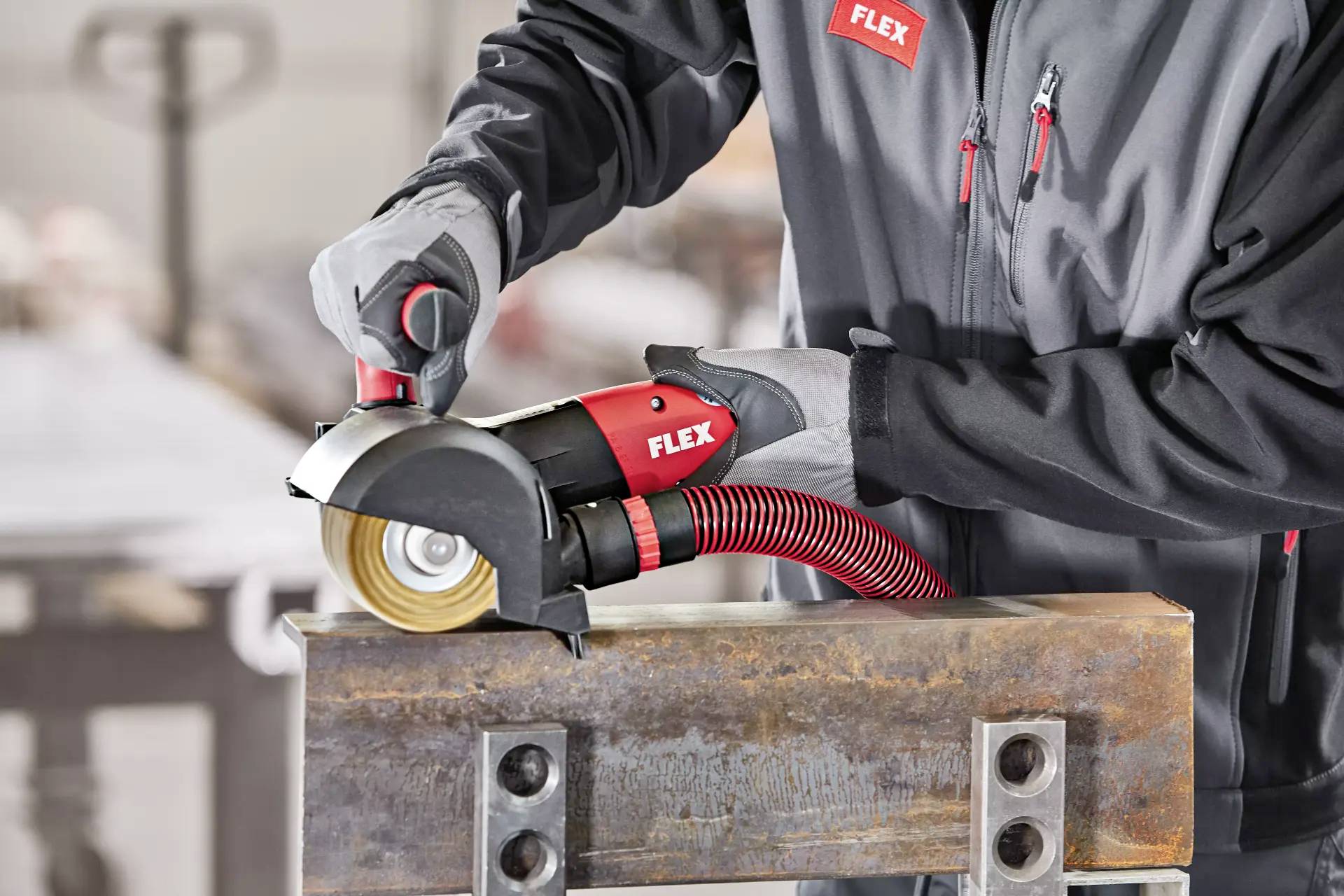 Osoba w odzieży ochronnej szlifuje kawałek metalu czerwono-czarną szlifierką kątową w środowisku warsztatu.