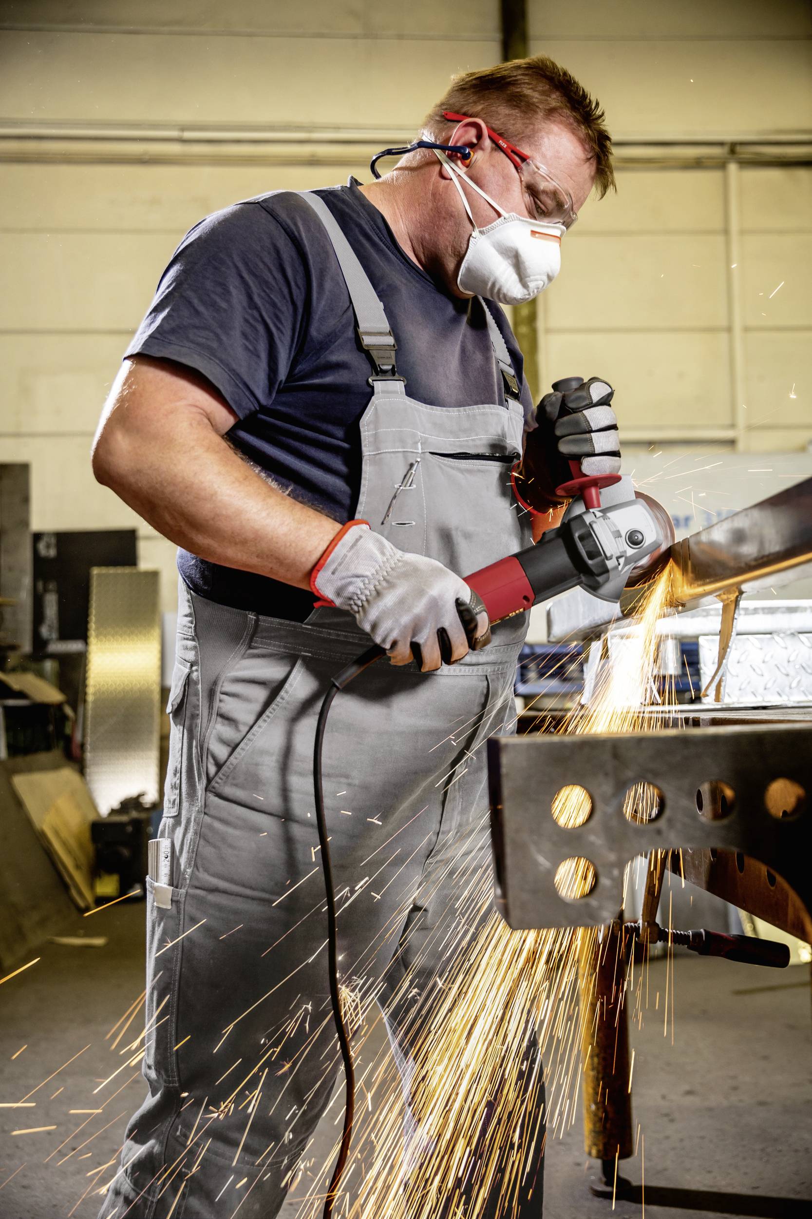 Pracownik w odzieży ochronnej szlifuje metal szlifierką kątową, iskry lecą. Bezpieczeństwo w miejscu pracy jest ważne.