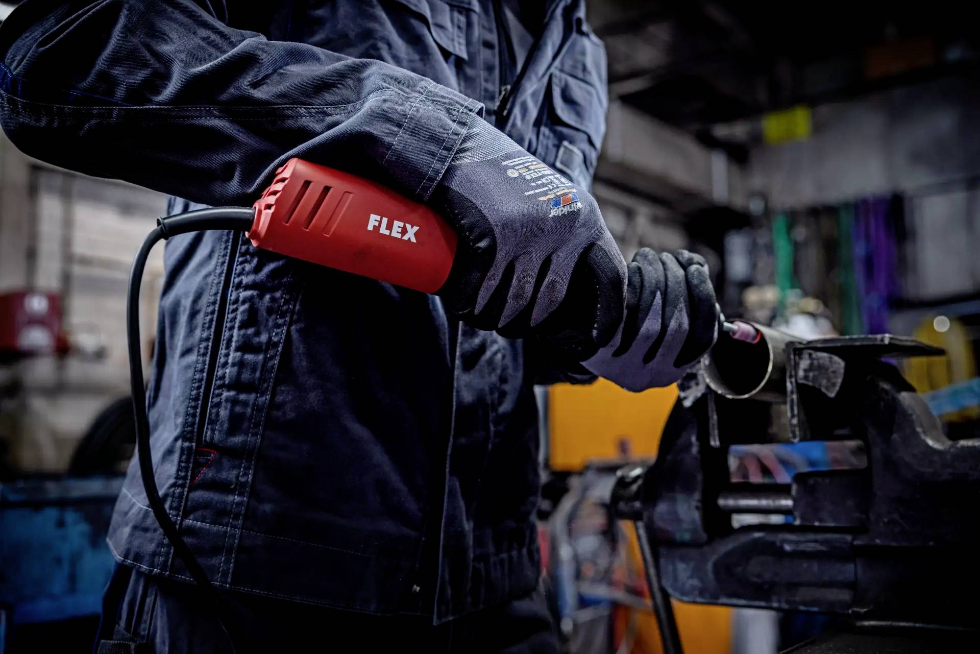 Osoba ubrana w odzież roboczą używa elektrycznej szlifierki kątowej do obróbki metalowej rury w warunkach warsztatowych.