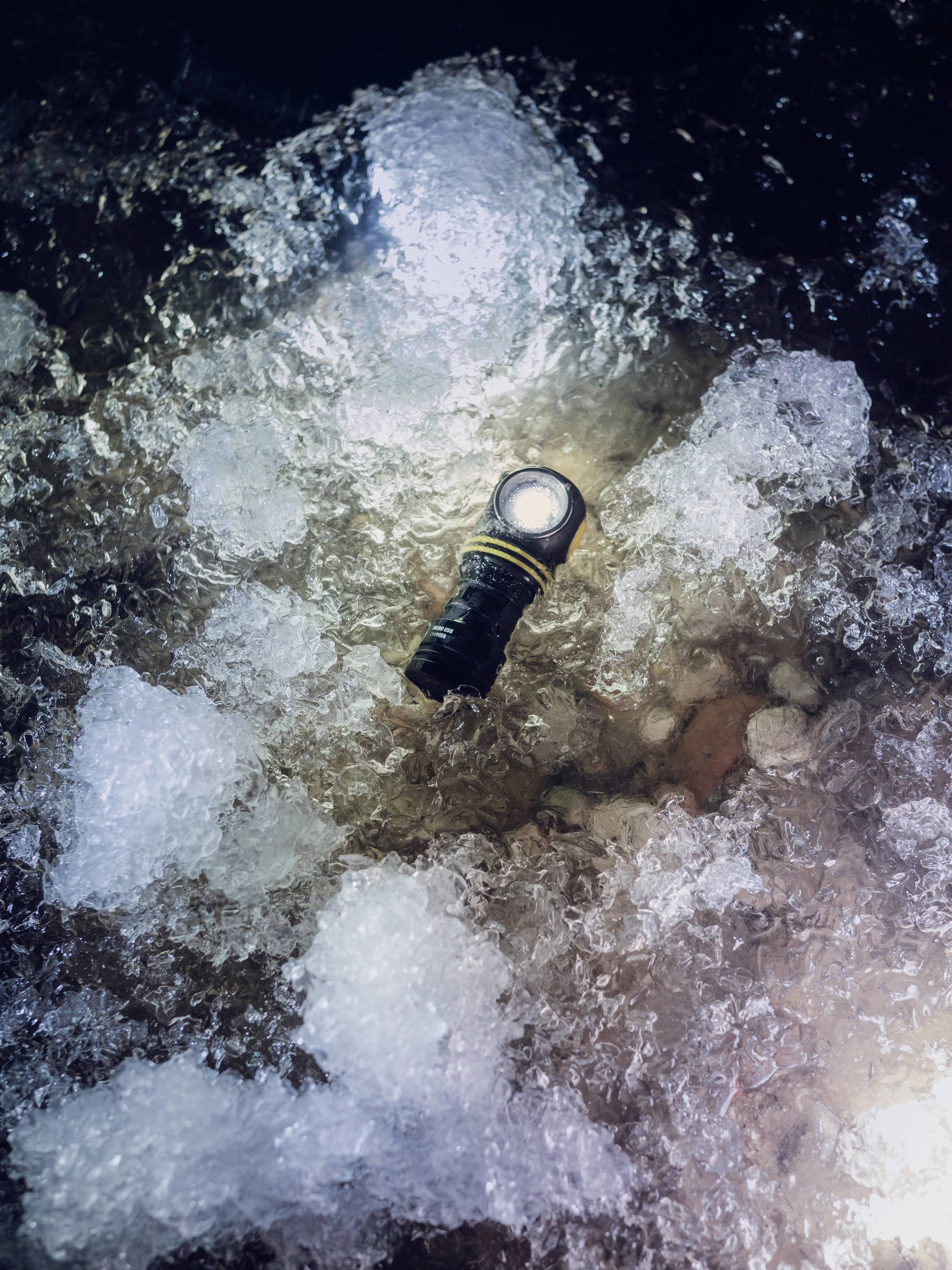 Włączona latarka, leżąca na lodzie, lekko świeci w górę.