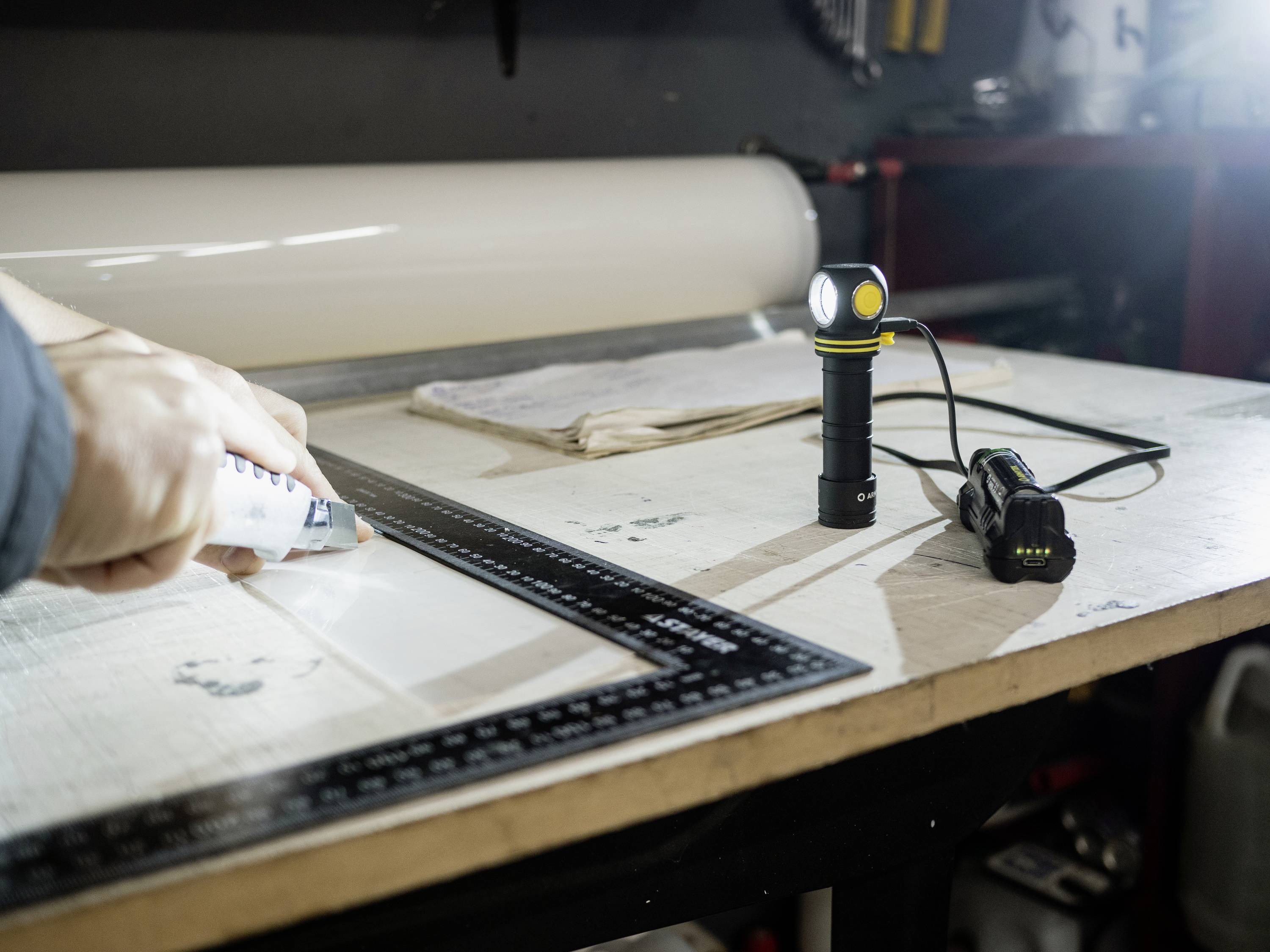 Osoba przykleja coś pistoletem do kleju na powierzchni roboczej. Obok leżą latarka i linijka, które pomagają w pracy.