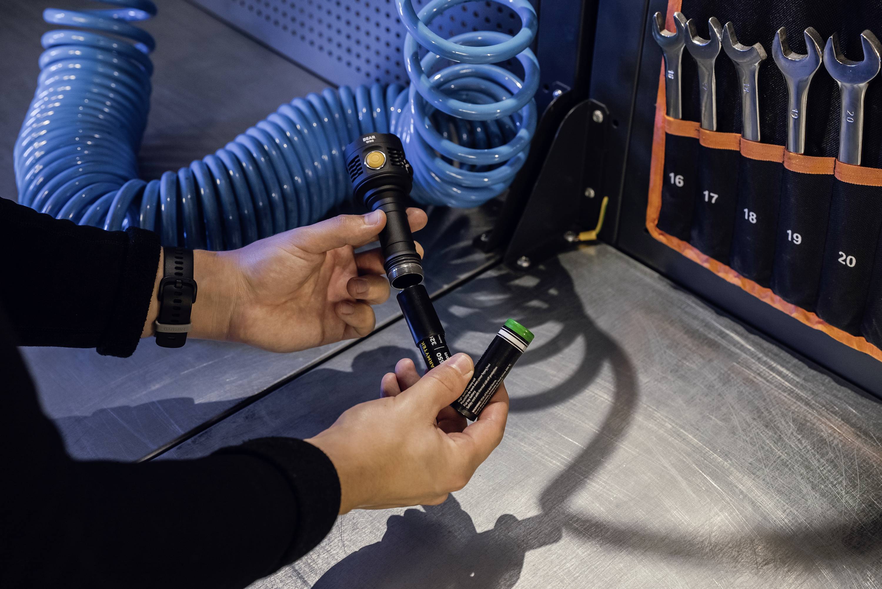 Ręce łączą czarne narzędzie z niebieskim kablem spiralnym w warsztacie, obok leży etui z ponumerowanymi kluczami.