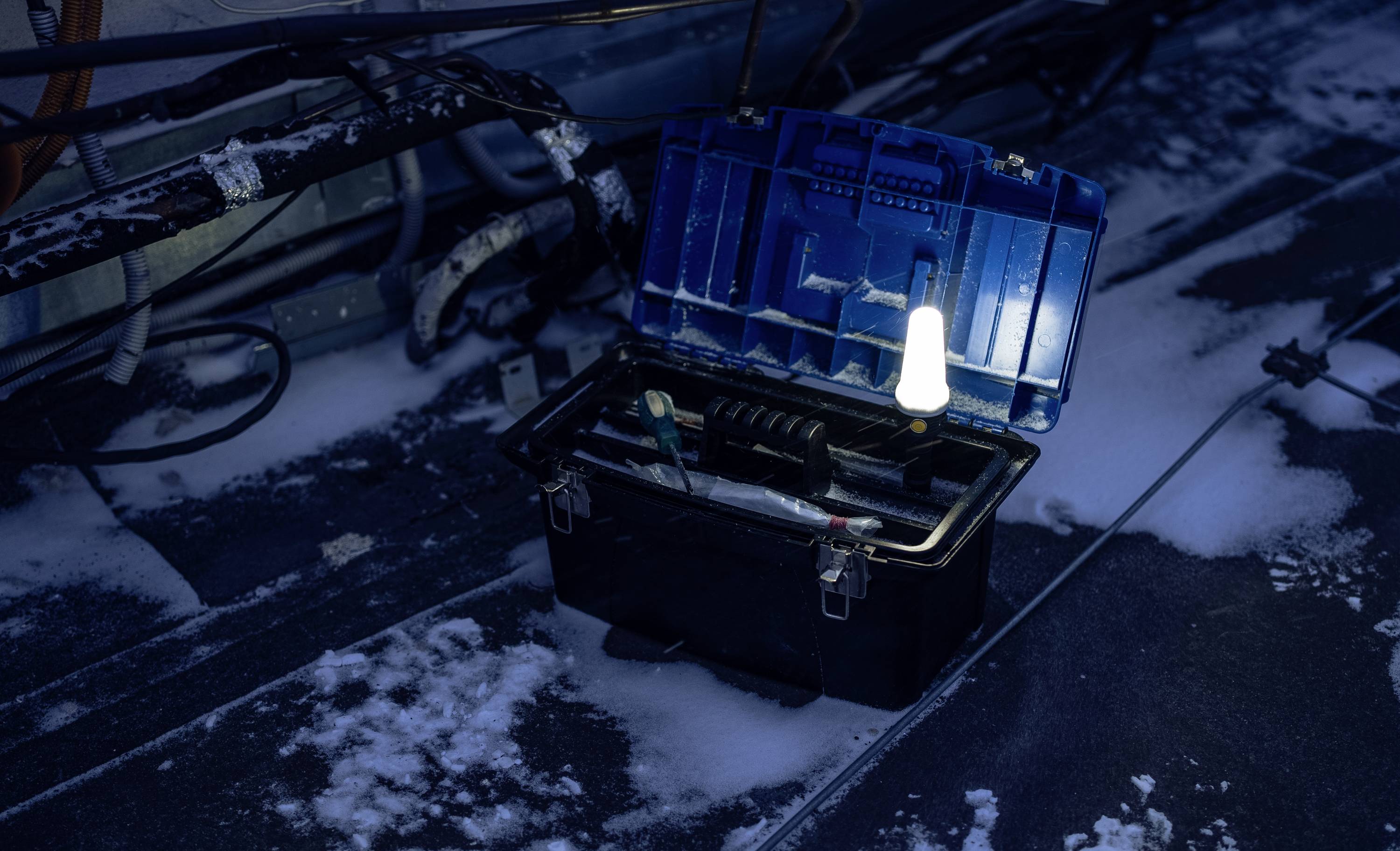 Otwarty skrzynka narzędziowa z różnymi narzędziami stoi na ośnieżonej ziemi. W tle widoczne są kable.