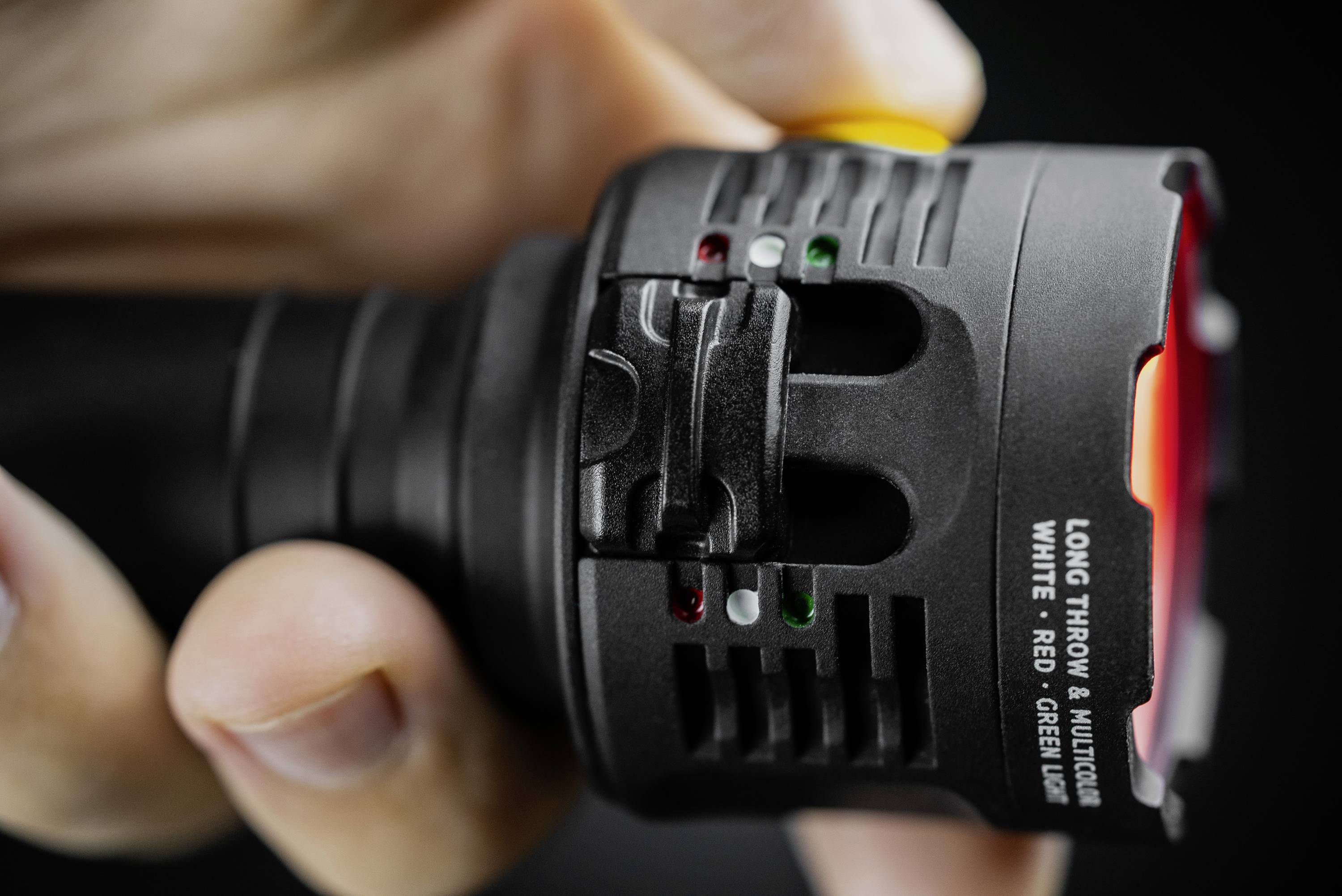 Zbliżenie dłoni trzymającej latarkę. Latarka posiada wskaźniki świetlne i przełączniki do wyboru różnych kolorów światła.