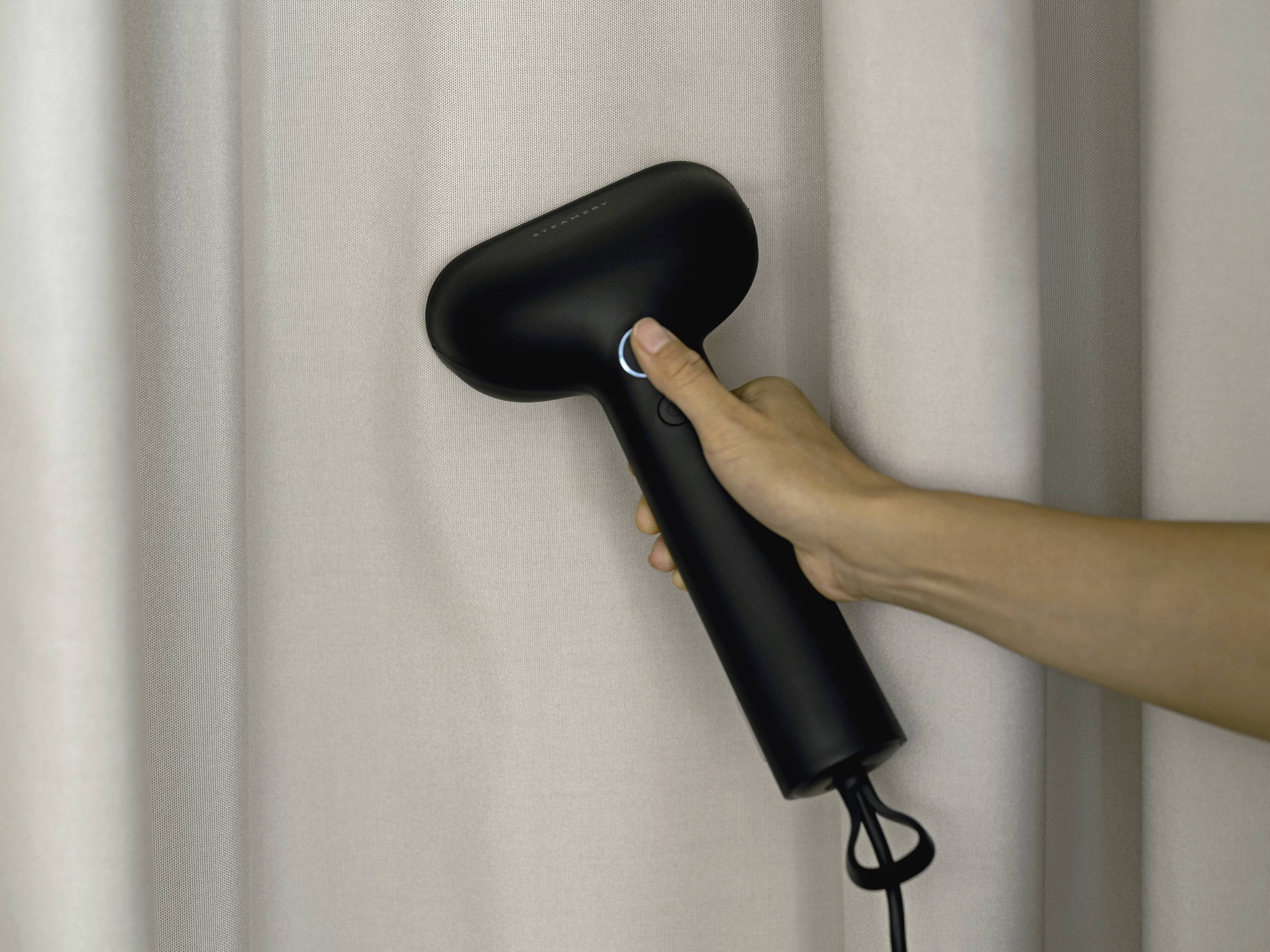 Ręka trzyma żelazko parowe wygładzające zasłonę.