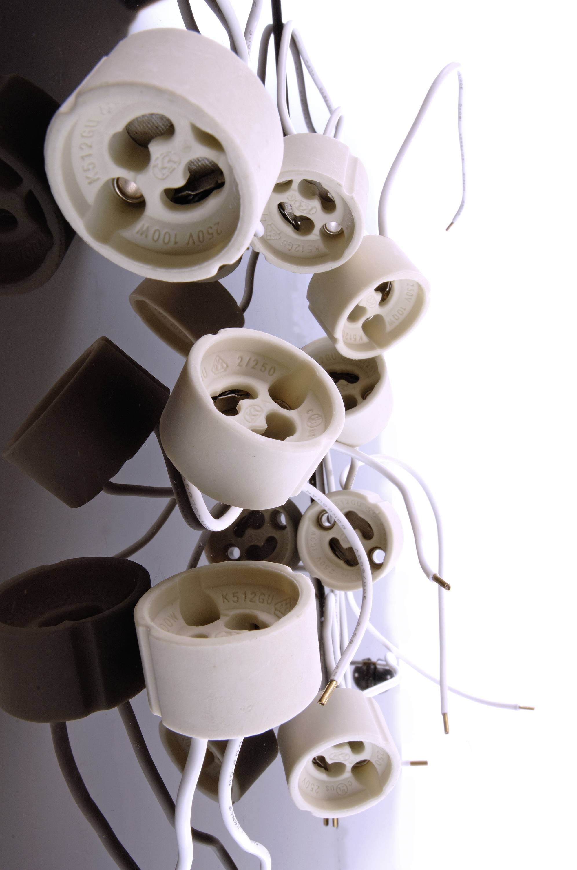 Kilka ceramicznych oprawek lamp z odsłoniętymi przewodami wisi luźno na białej ścianie, bez podłączonych żarówek.