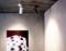 Dwa reflektory sufitowe oświetlają ścianę z dziełem sztuki przedstawiającym rolki filmowe. Scena jest utrzymana w nowoczesnym i minimalistycznym stylu.