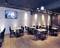 Nowoczesna restauracja z drewnianą podłogą, białymi ścianami z cegły i czarnymi krzesłami. Puste stoły ustawione są w rzędach, a na ścianie wisi ekran.