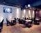Nowoczesna restauracja z drewnianą podłogą, białymi ścianami z cegły i płaskim telewizorem zamontowanym na ścianie. Stoły i krzesła są równomiernie rozmieszczone.