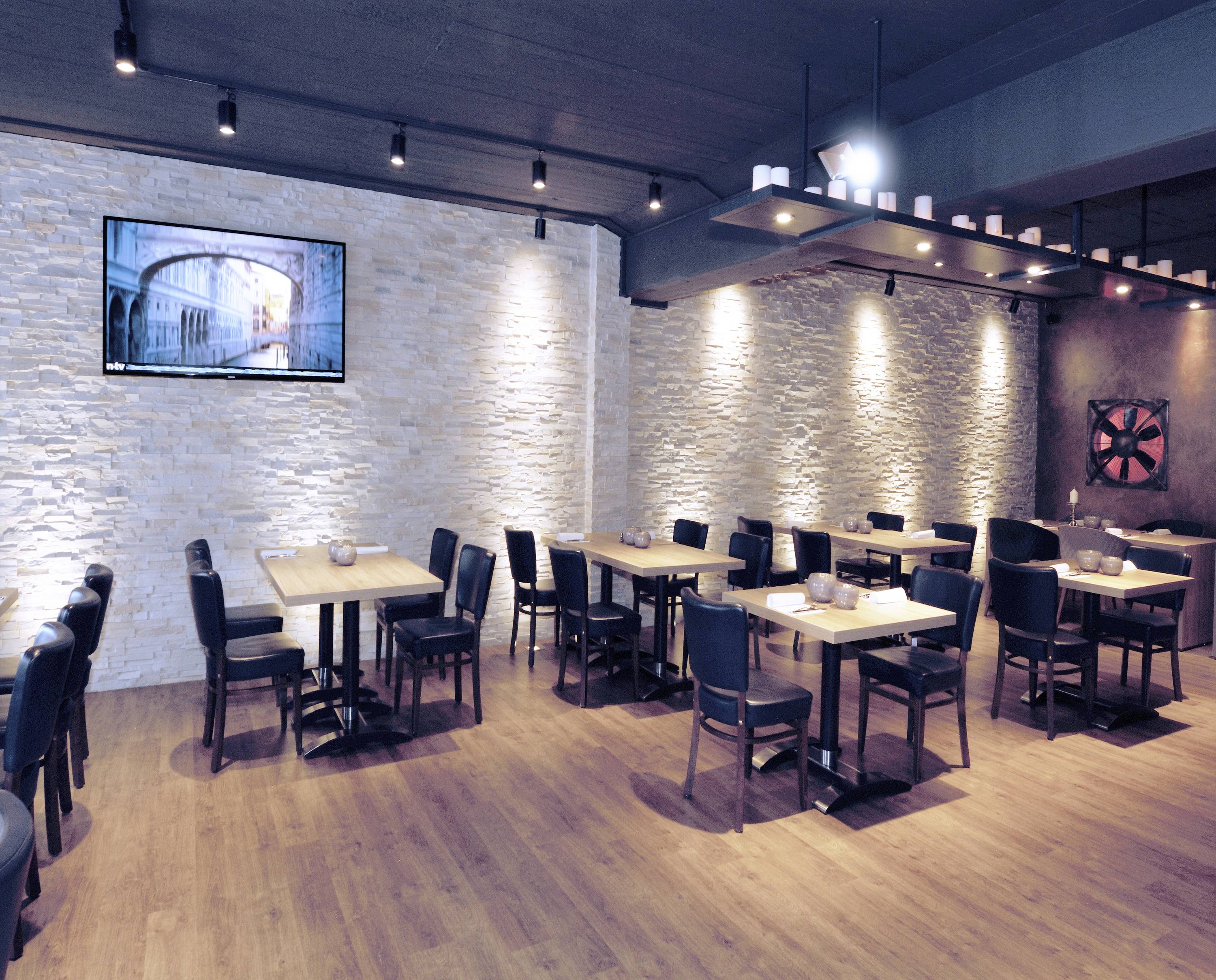 Pusty, nowoczesny salon restauracyjny z drewnianymi stołami i czarnymi krzesłami. Na ścianie wisi płaski telewizor.