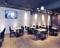 Pusty, nowoczesny salon restauracyjny z drewnianymi stołami i czarnymi krzesłami. Na ścianie wisi płaski telewizor.