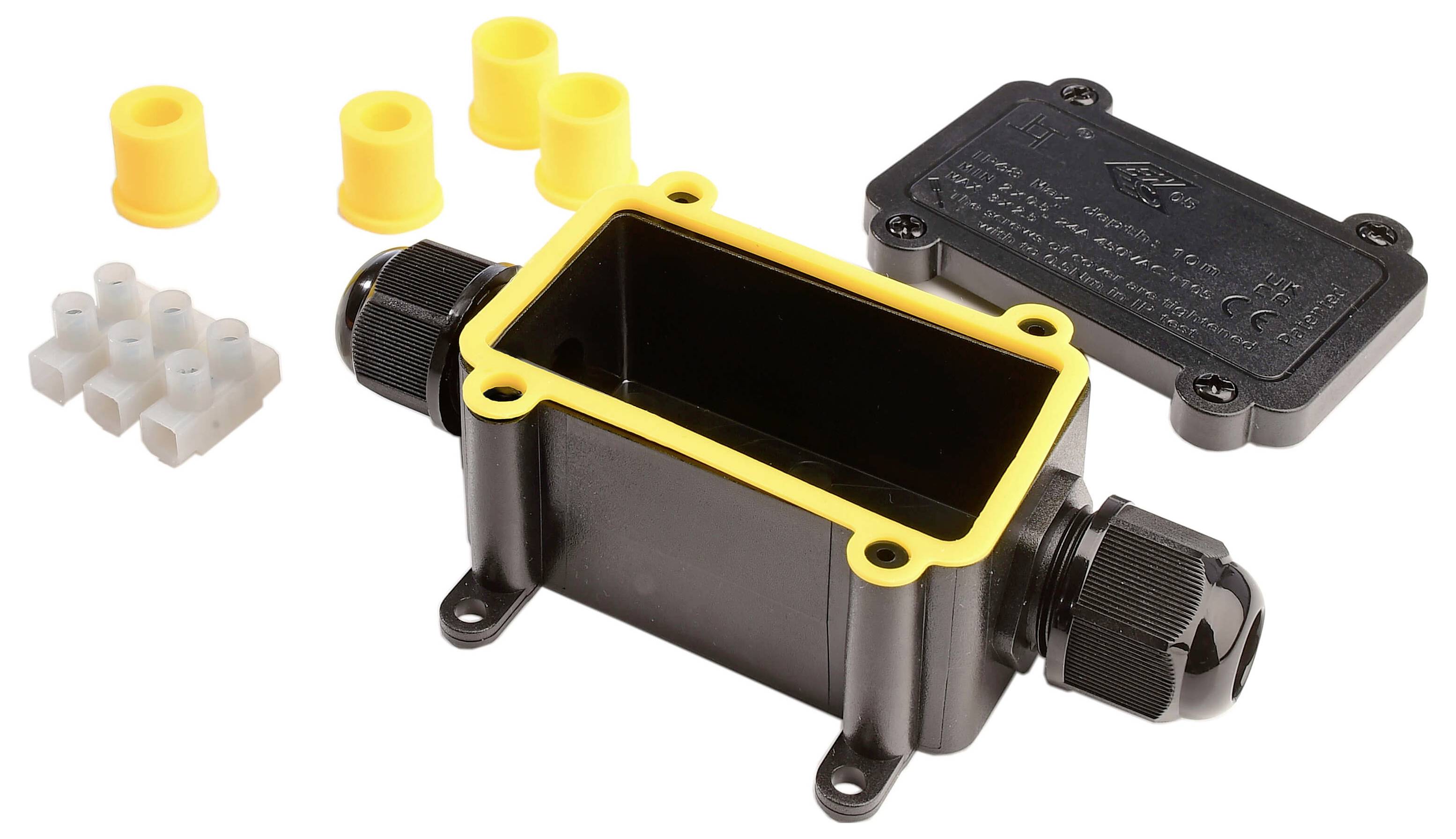 Czarna puszka przyłączeniowa z żółtą krawędzią i dławicami kablowymi, z zdjętą pokrywą. Zawiera akcesoria: żółte uszczelki gumowe i białą listwę zaciskową.