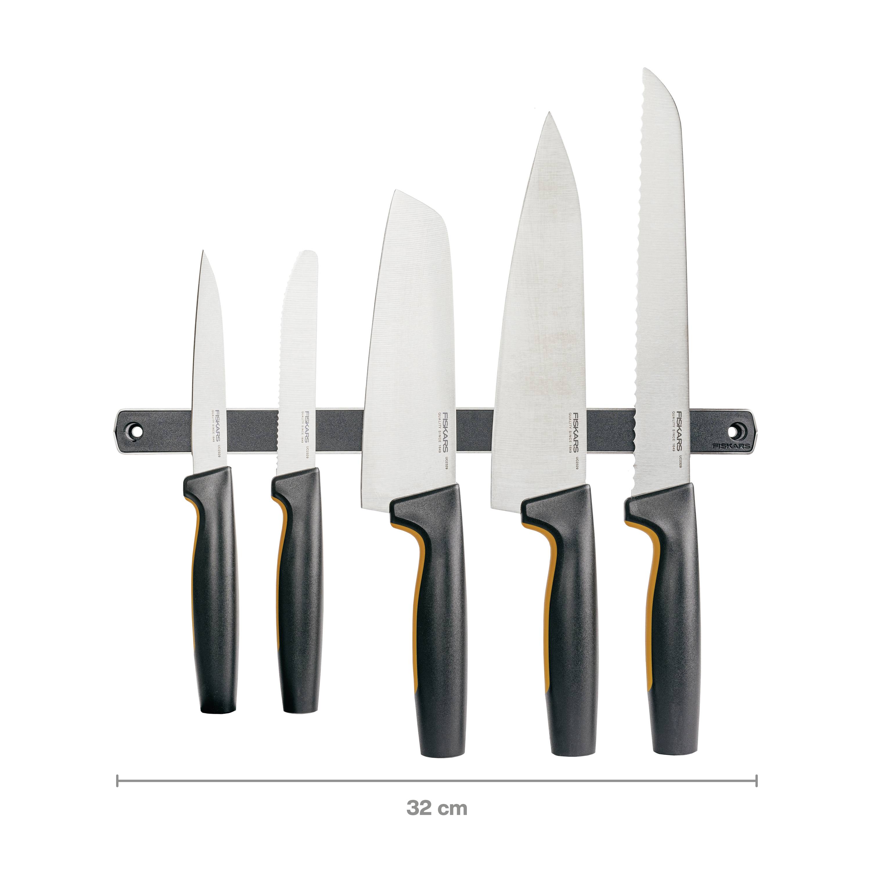 'Pięć noży kuchennych z czarnymi uchwytami, zamocowanych na magnetycznym stojaku, ułożonych od najmniejszego do największego noża.'