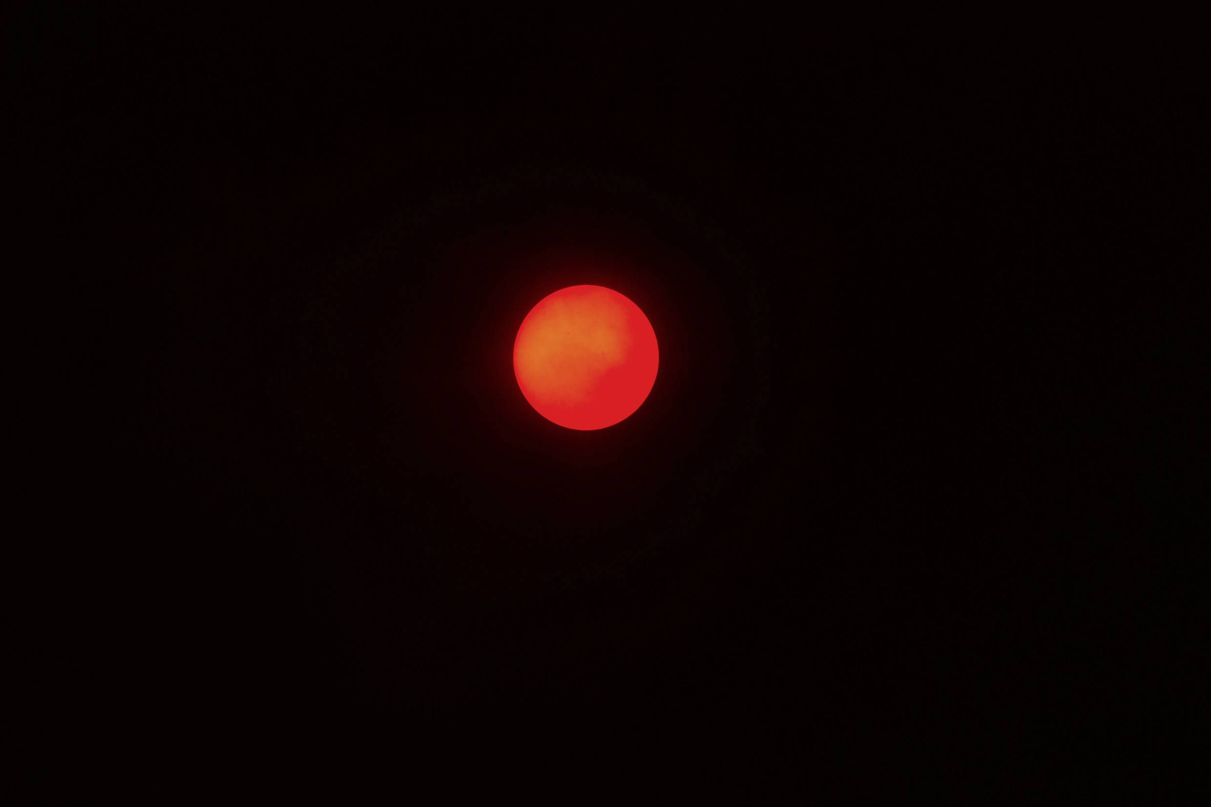 Czerwona, świecąca pełnia księżyca na nocnym niebie, otoczona ciemnością.