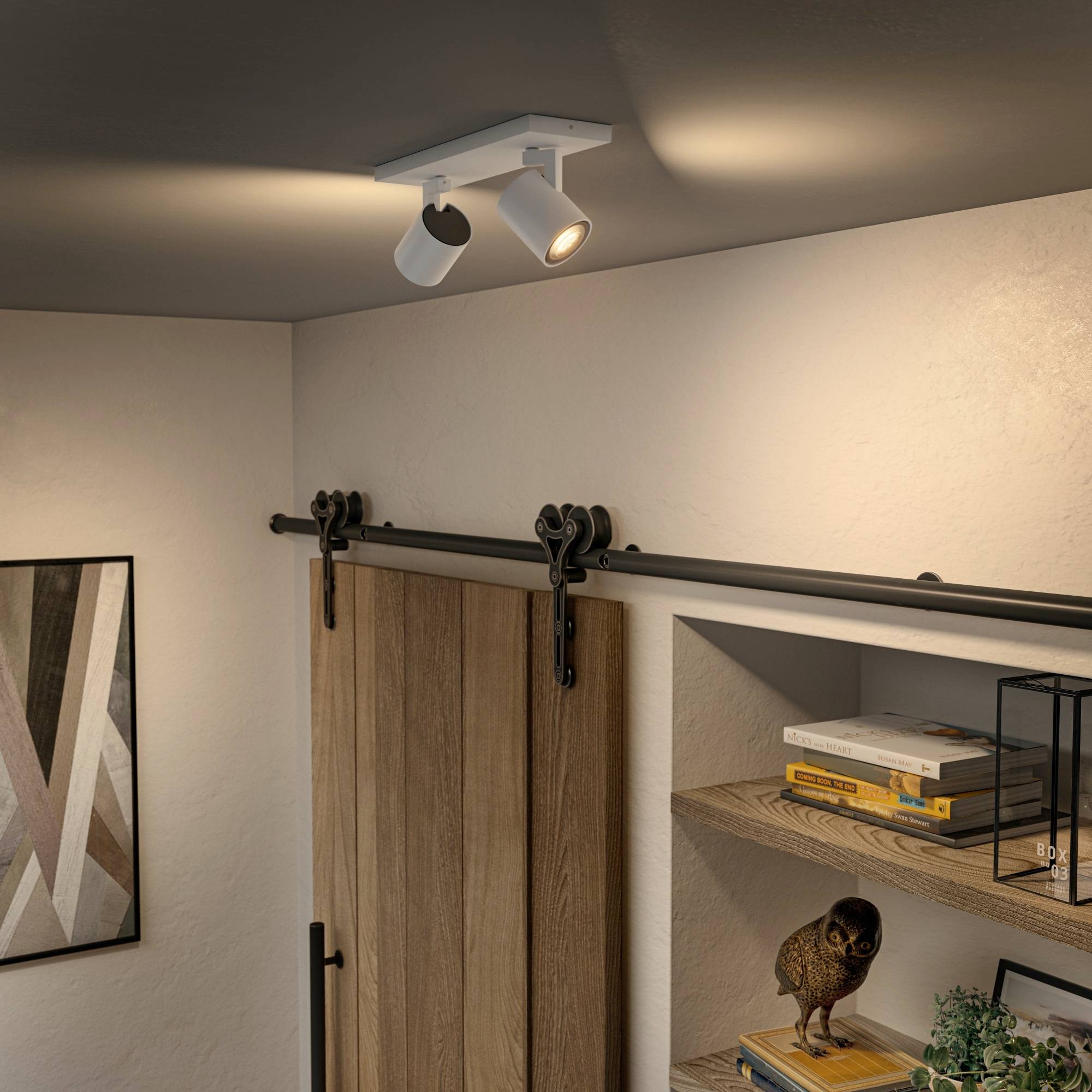 Minimalistyczny salon z obrotowym reflektorem, obrazem na ścianie, drewnianą półką z książkami i dekoracyjną figurką sowy.