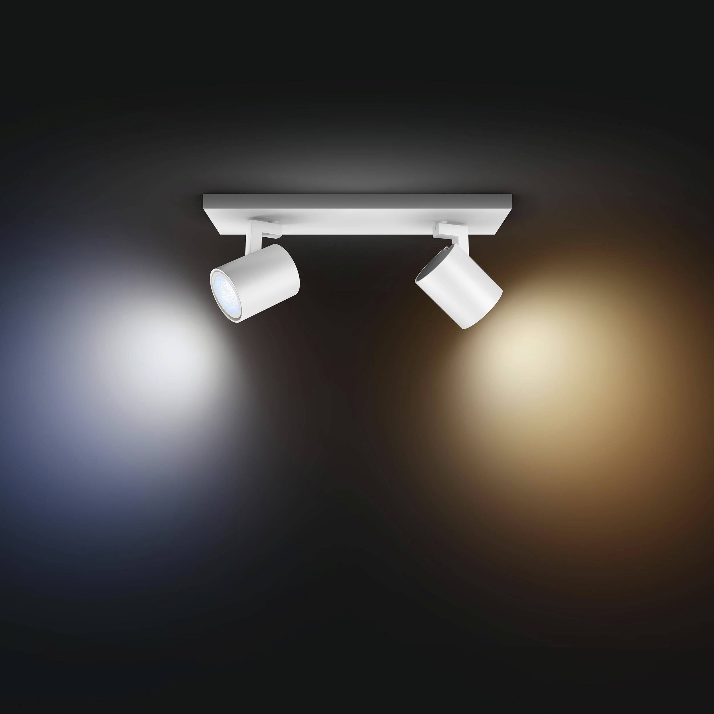 Lampa sufitowa z dwoma regulowanymi reflektorami, jeden emituje białe, drugi ciepłożółte światło, na czarnym tle.