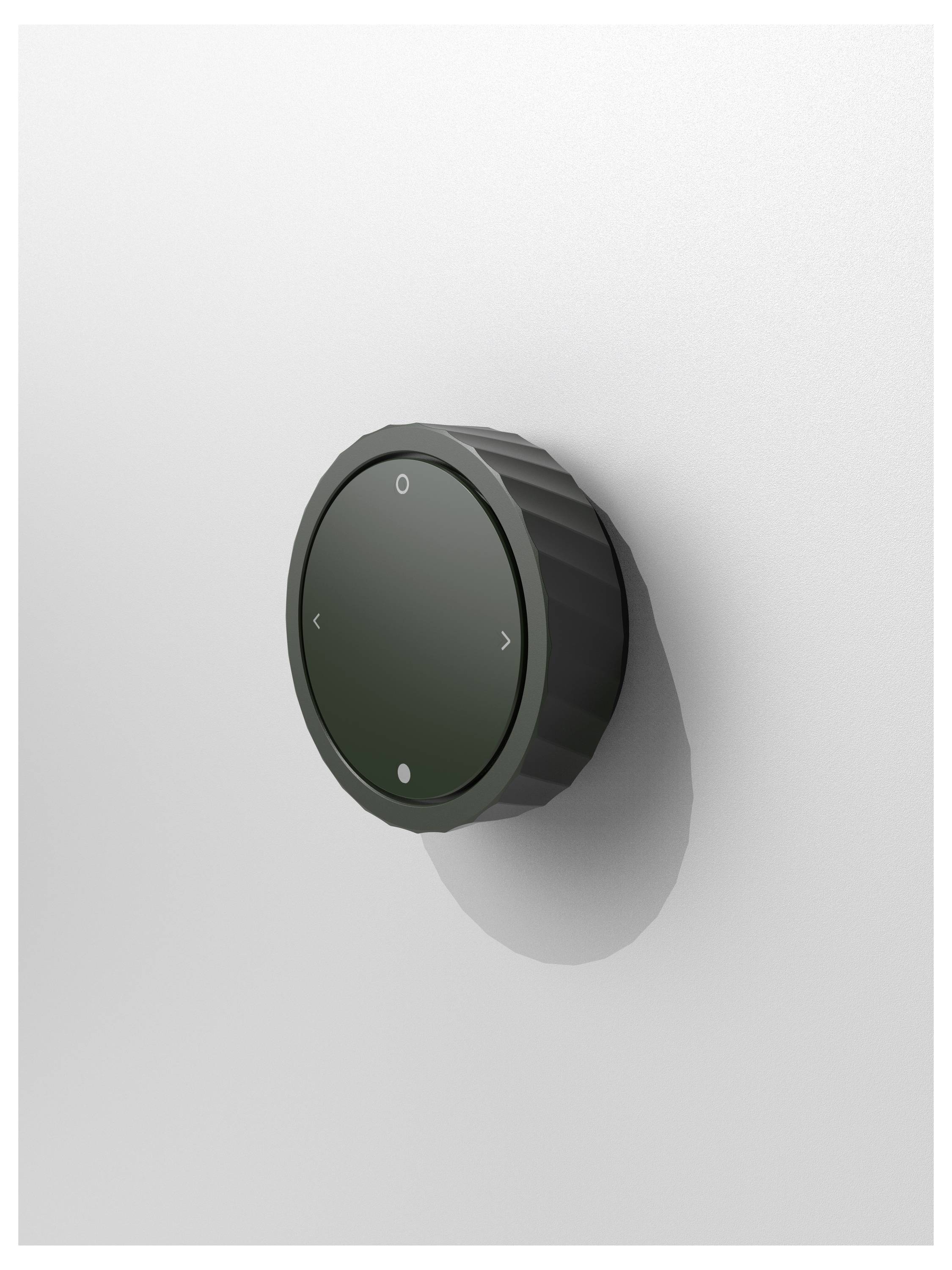 Czarny, okrągły pokrętło na białej ścianie, z czterema strzałkami wskazującymi kierunki, prawdopodobnie do regulacji głośności.