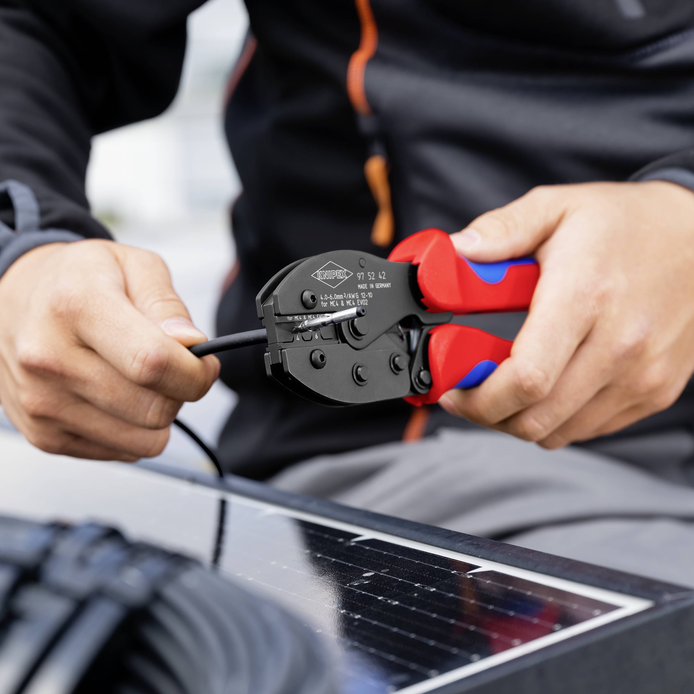 Osoba używa czerwonej zaciskarki do pracy przy kablu obok panelu słonecznego.