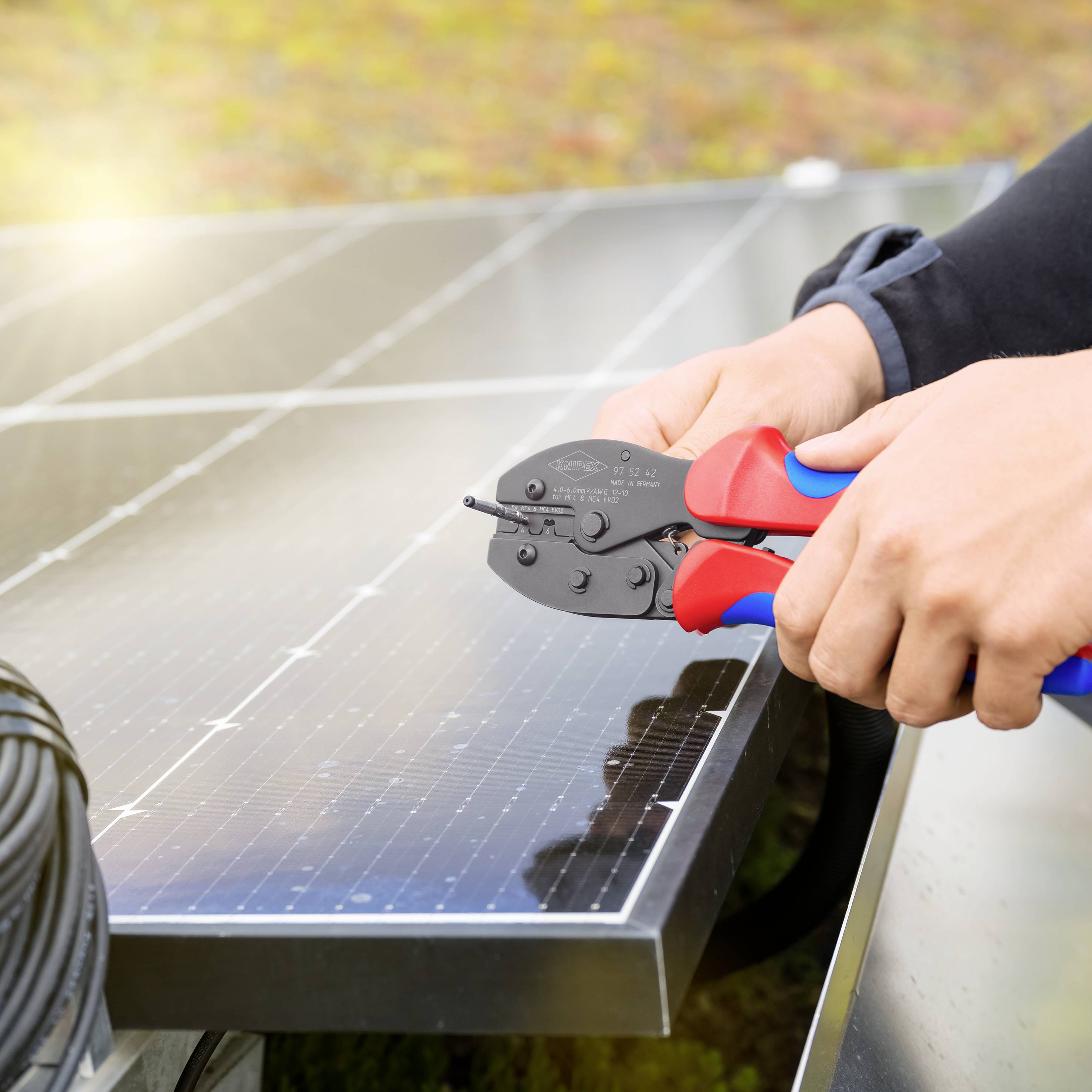 Osoba instaluje moduły solarne na dachu, używając narzędzia do łączenia kabli, przy czym światło słoneczne się odbija.