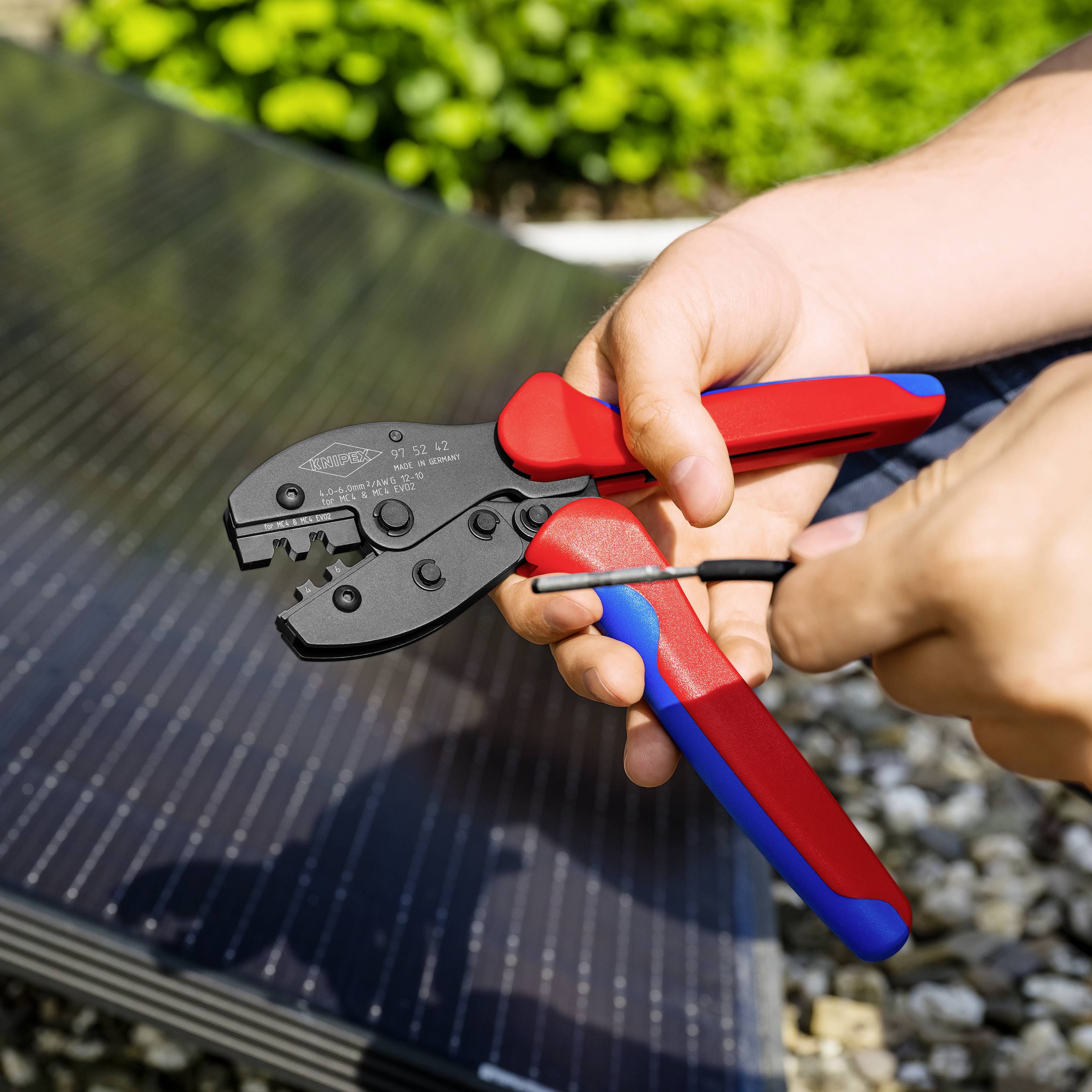 Osoba trzyma zaciskarkę i pracuje przy panelu słonecznym. Scena przedstawia rzemieślniczą czynność na wolnym powietrzu.