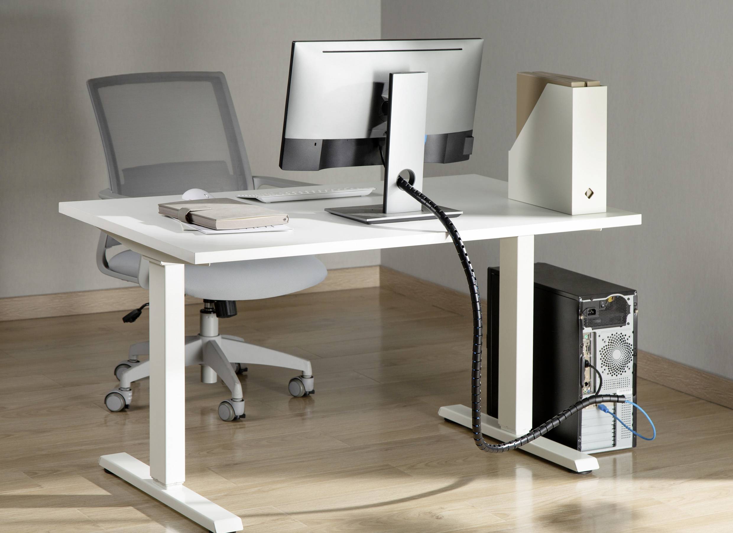 Nowoczesne stanowisko biurowe z białym biurkiem, ergonomicznym fotelem, monitorem, zamkniętym laptopem, pionowo ustawionym obudowaniem komputera i zarządzaniem kablami, na jasnej podłodze laminowanej.