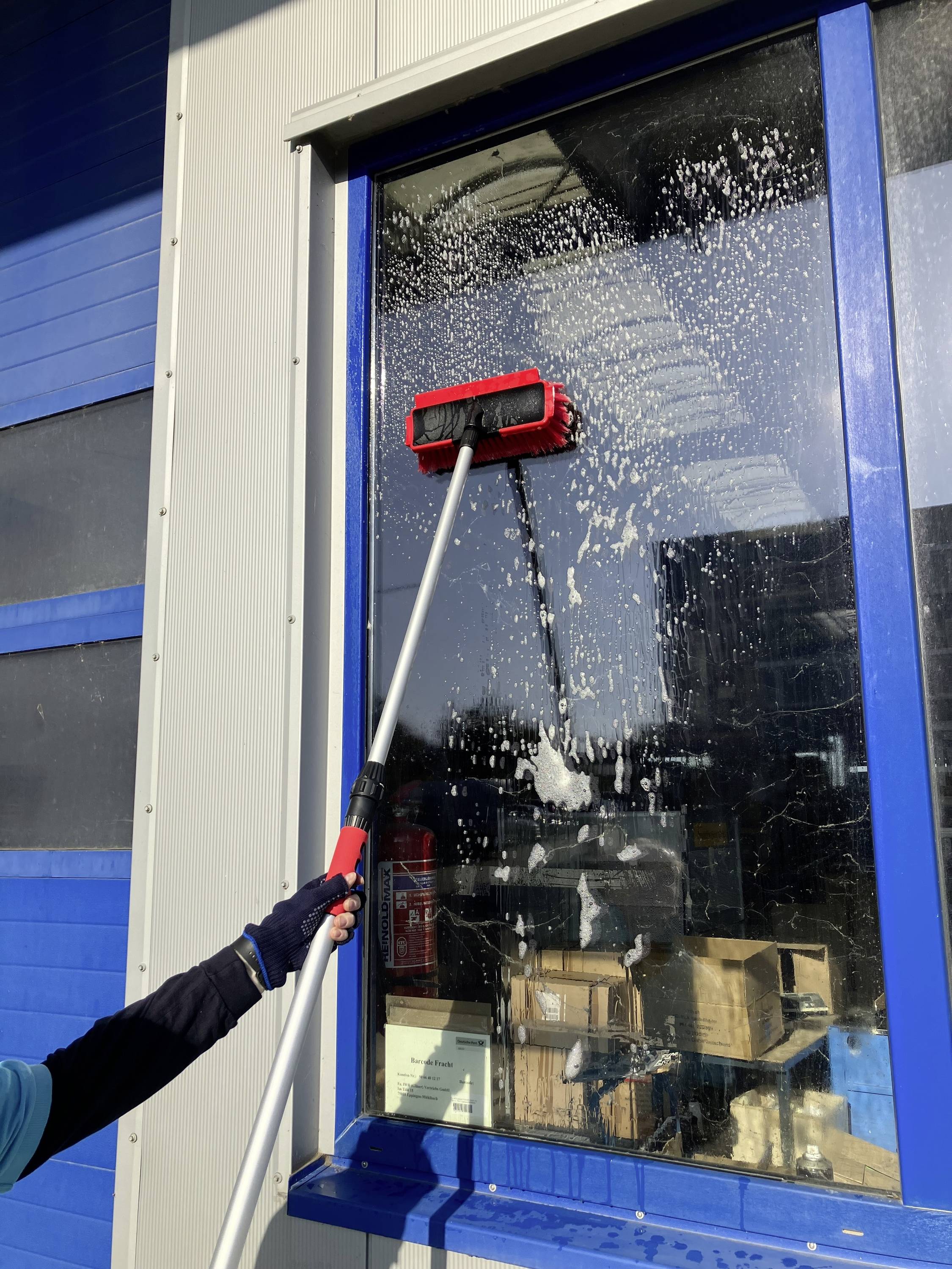 'Jedna osoba myje duże okno długą szczotką i wodą z mydłem w słoneczny dzień.'