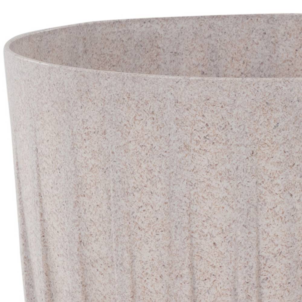 Beżowy, okrągły kubek o fakturze żłobień. Stoi na białym tle.