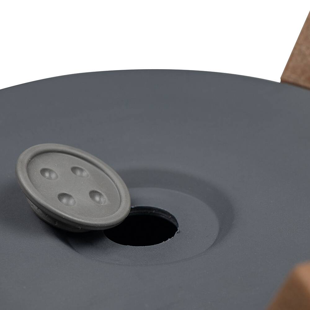 Ciemnoszara tarcza z wciskanym przyciskiem pośrodku. Na tle widoczny jest brązowy brzeg.