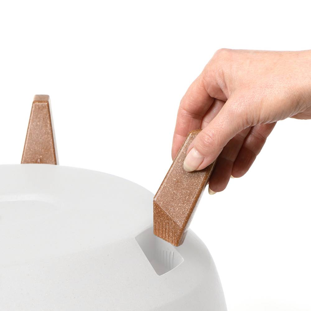 Dłoń umieszcza prostokątny, brązowy drewniany przedmiot w białym, odpowiednio ukształtowanym otworze.