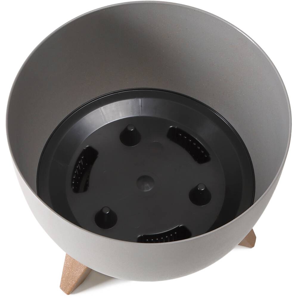 Okrągła doniczka z szarego plastiku z czarnymi wstawkami na dnie, stojąca na trzech drewnianych nogach.